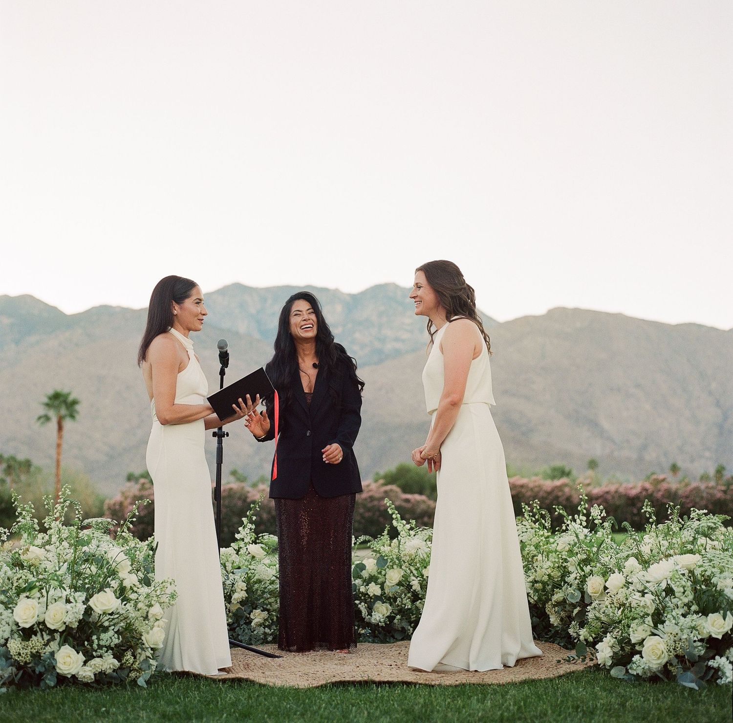 An outdoor wedding ceremony with white floral arrangements and mountain backdrop.