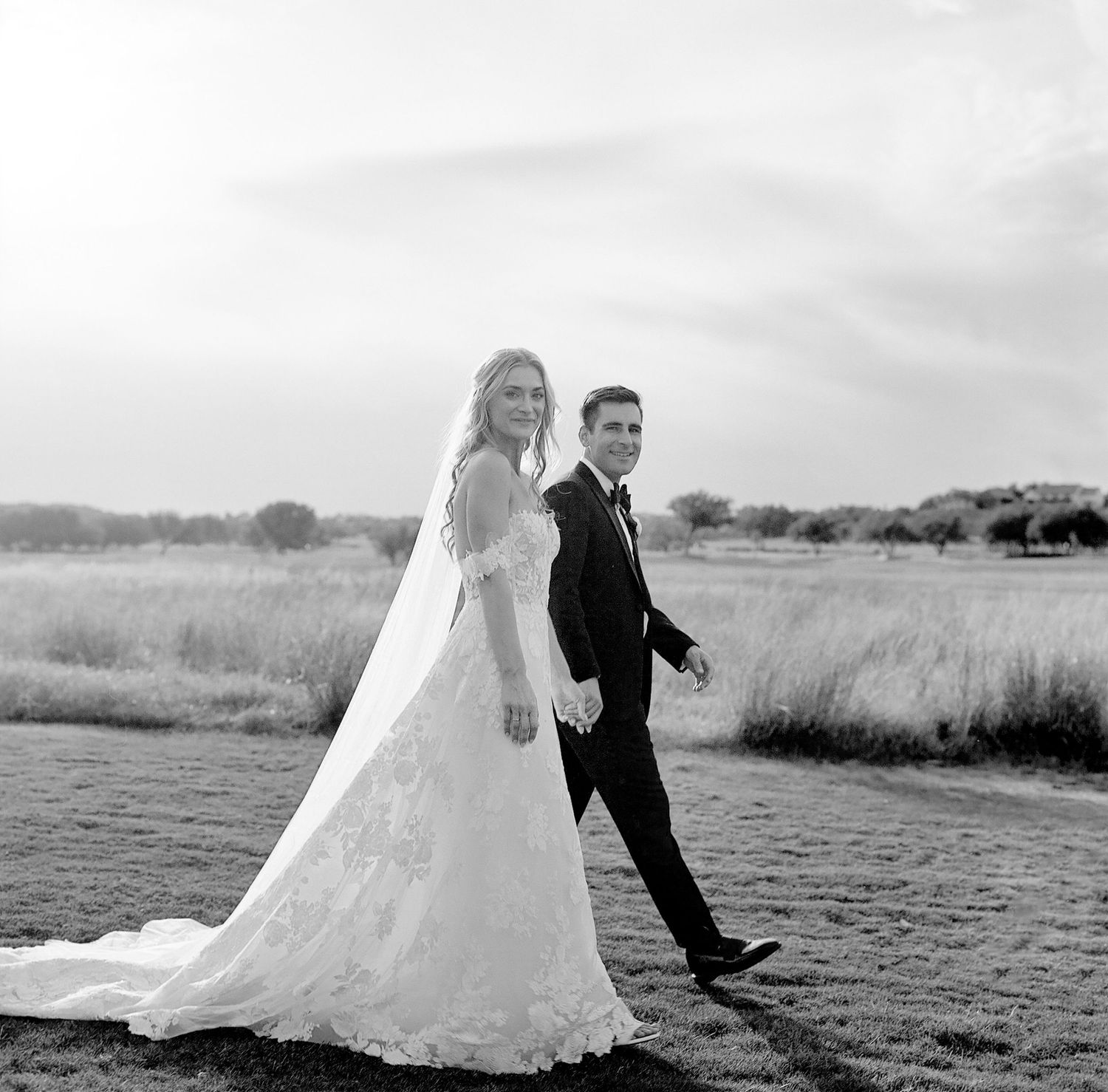Black and white photo of newlyweds walking together in an open field.
