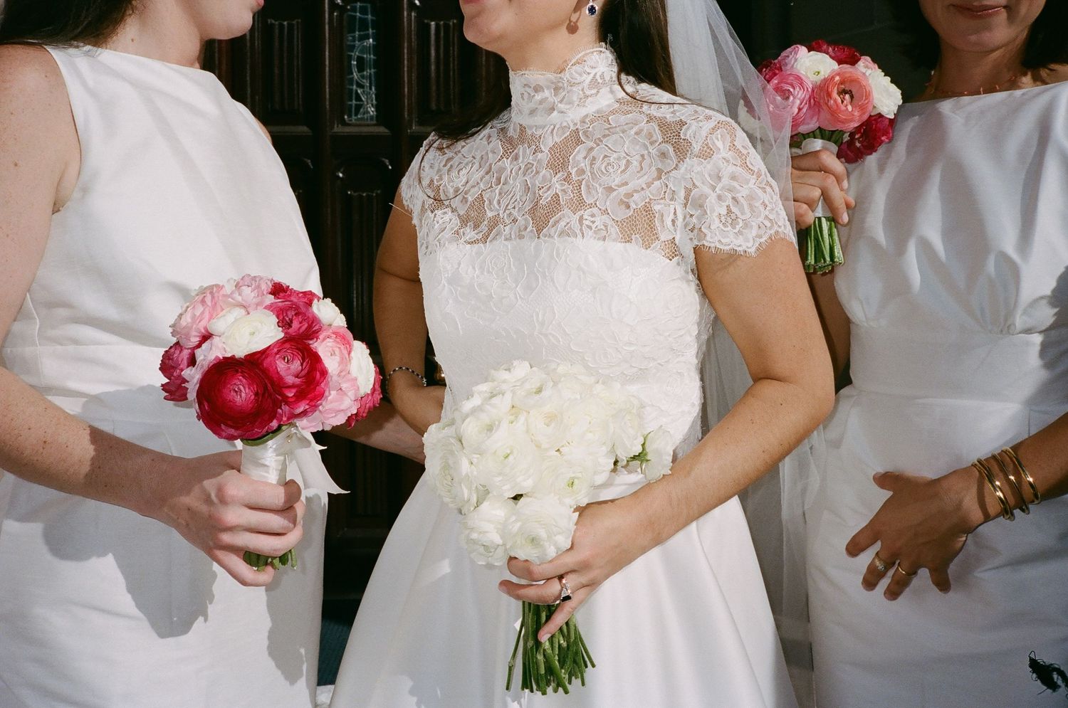 Wedding party members holding red and white bouquets in elegant white dresses.