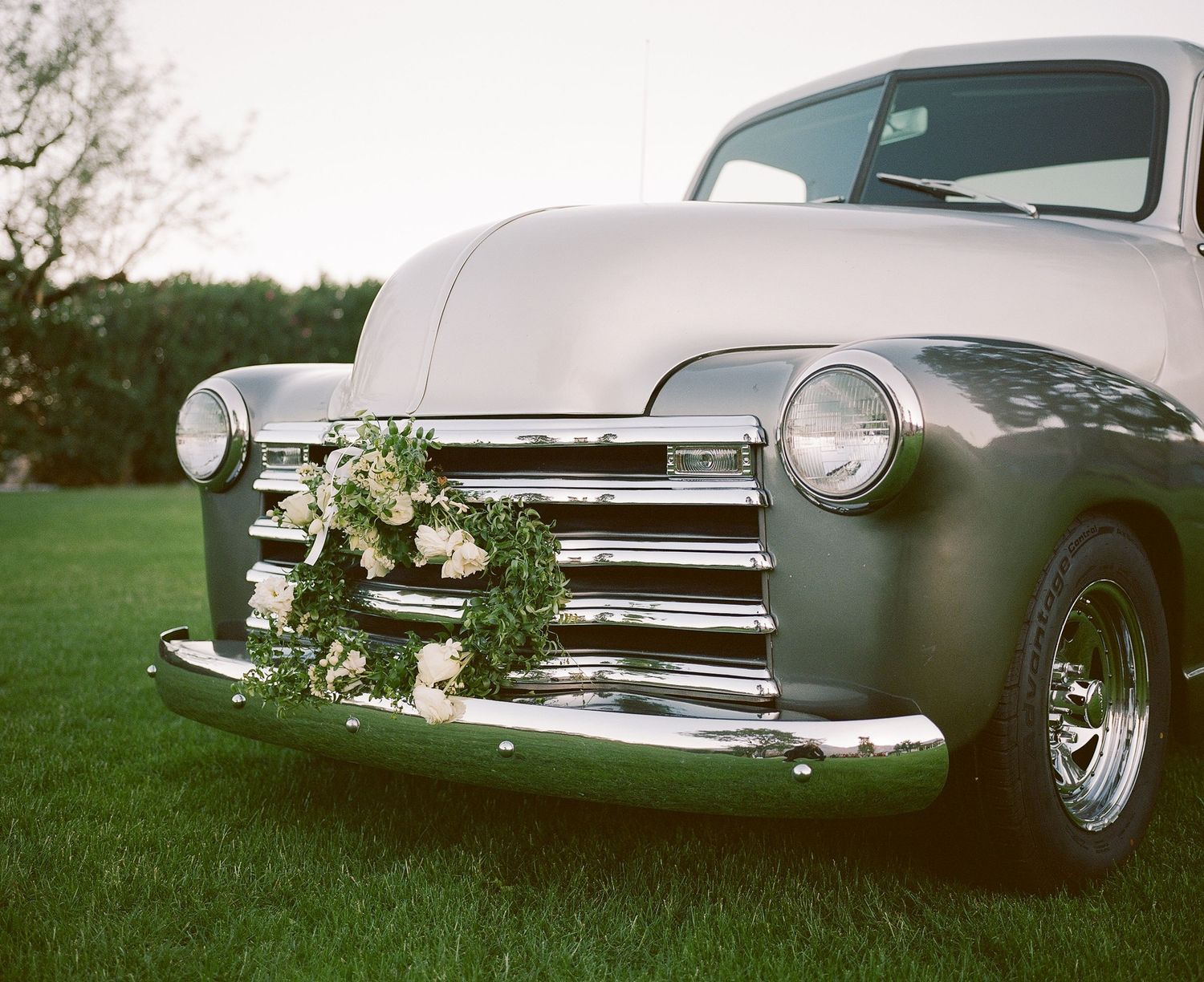 Classic vintage car decorated with greenery displayed at outdoor wedding venue.