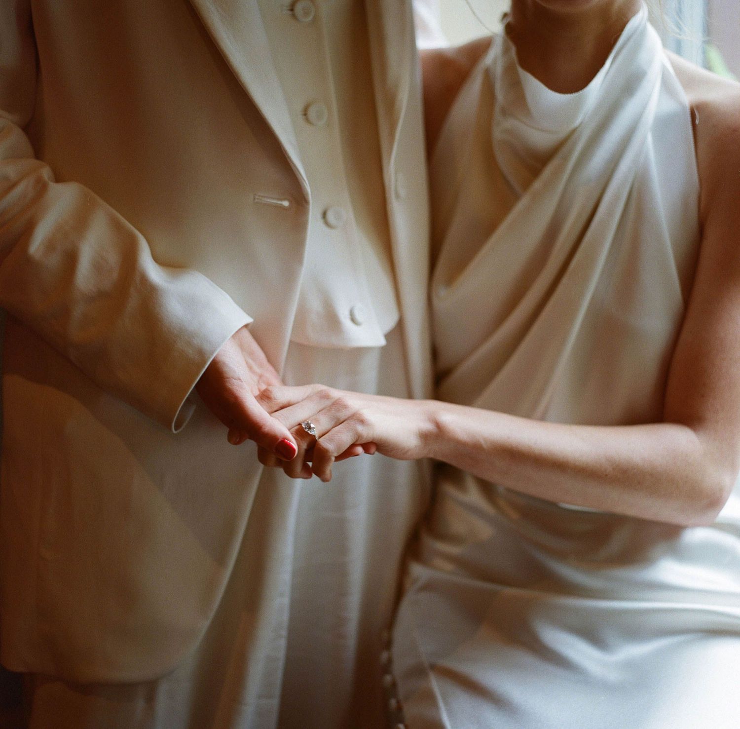 An intimate close-up of hands clasped together, both wearing elegant white formal wear.