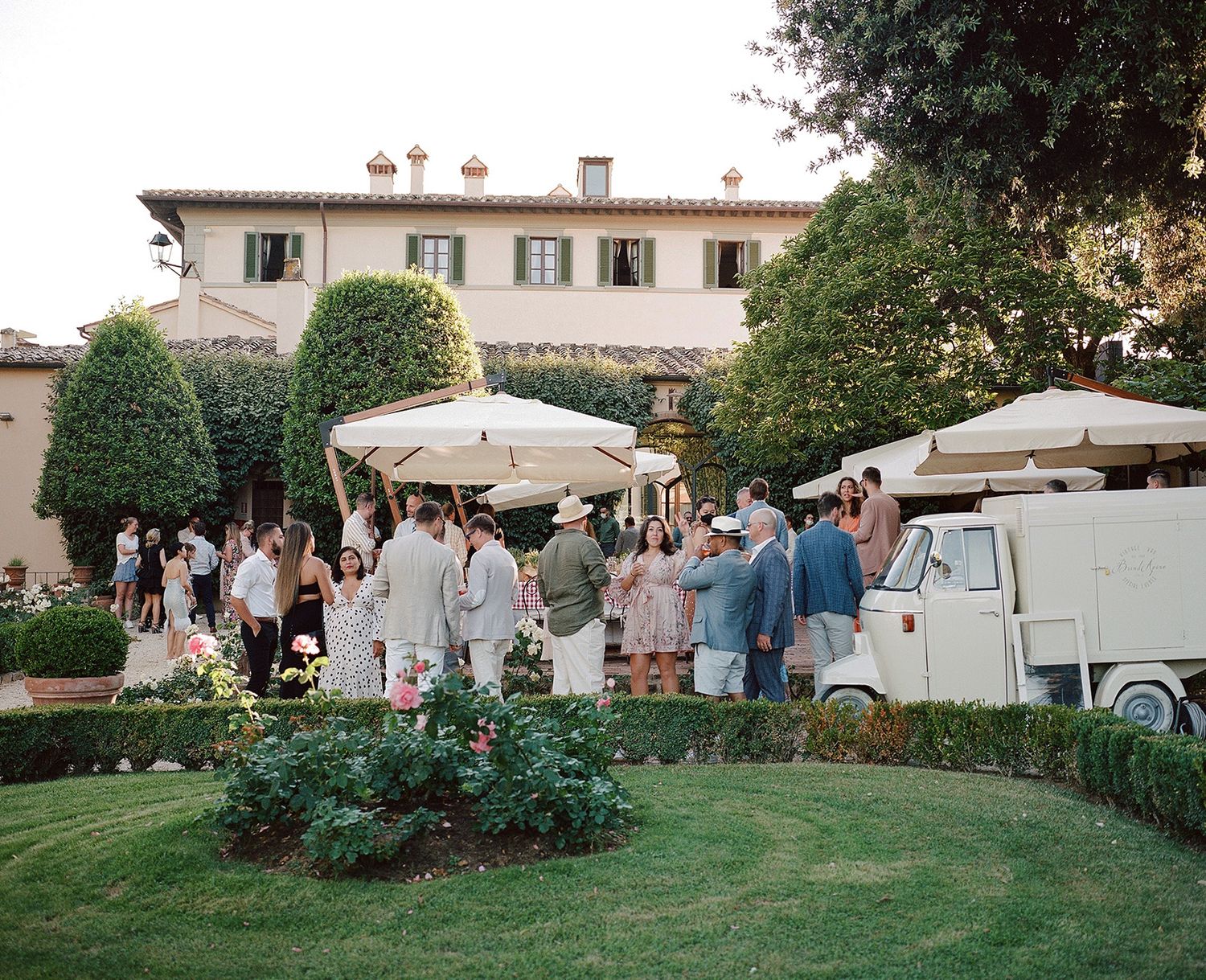 Outdoor garden reception with guests mingling on a manicured lawn at sunset.