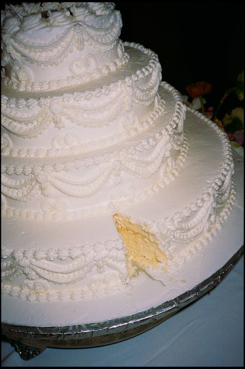 Elegant white multi-tiered wedding cake with intricate piped frosting details on a silver stand, with a slice removed.
