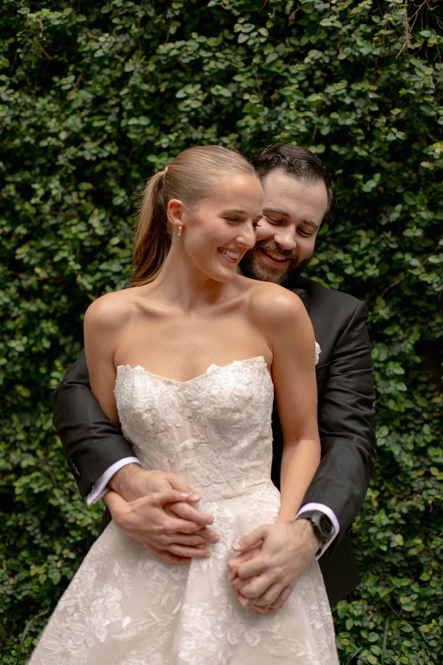 Wedding couple shares intimate moments in front of green foliage during outdoor photo session.