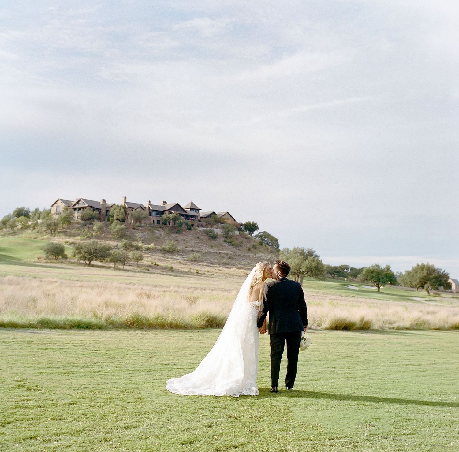 Wedding couple walking across a scenic green field with rolling hills in the background.