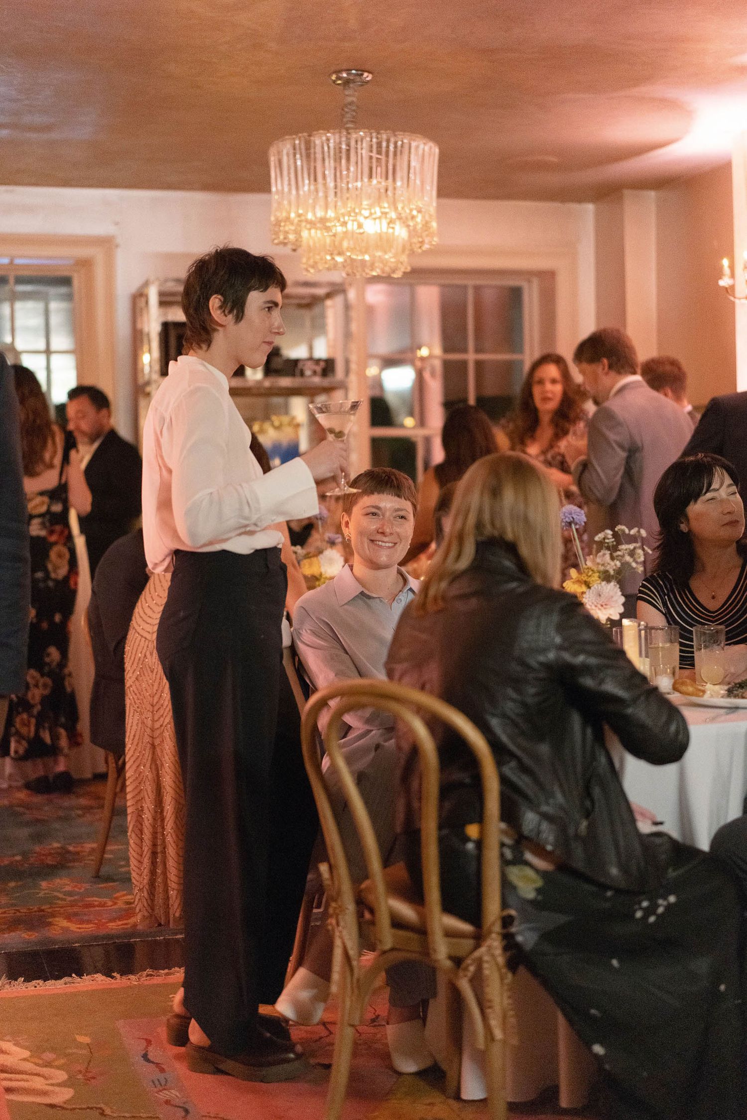 Wedding reception guests mingling and socializing under warm lighting and chandeliers.