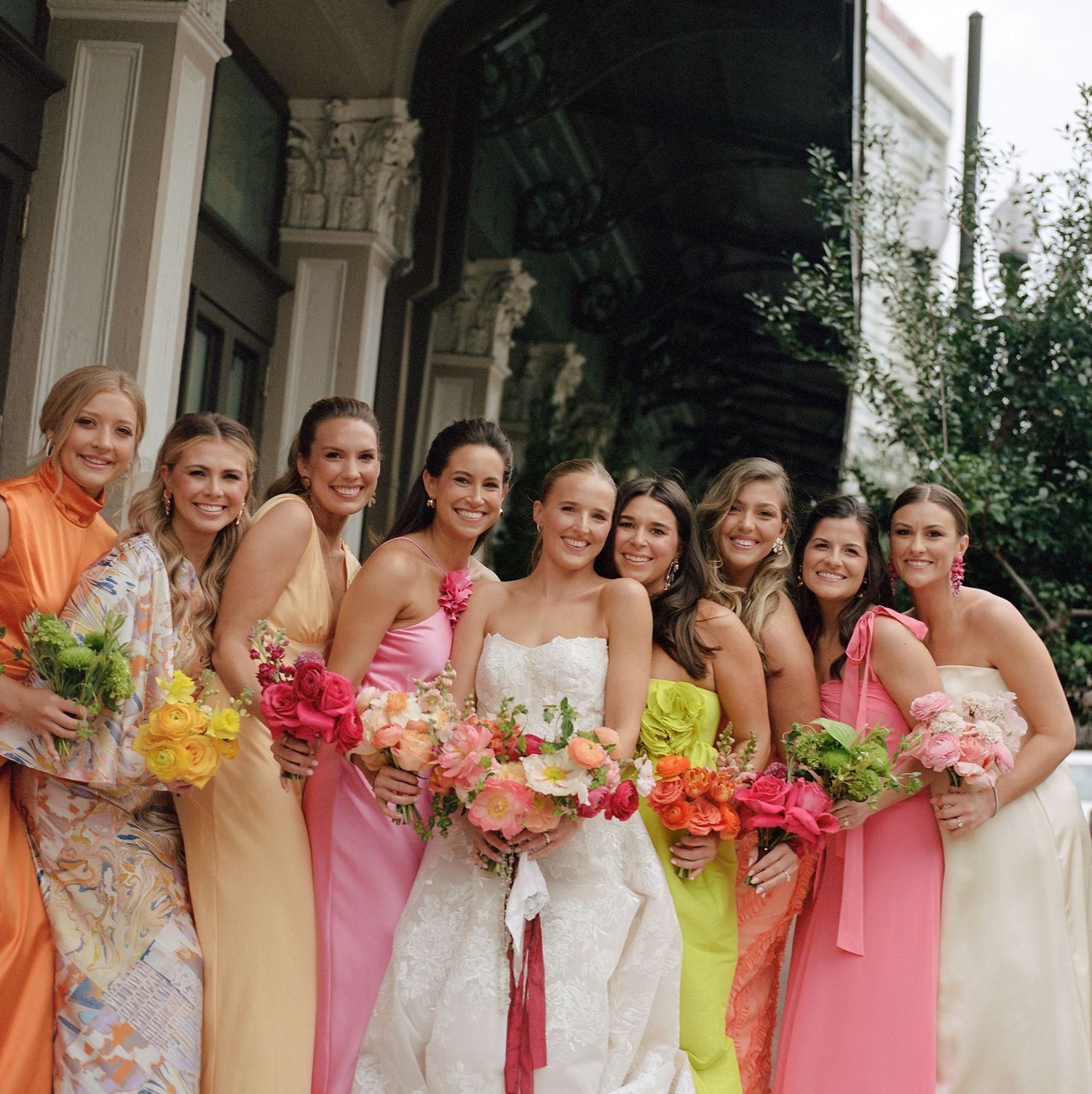 Wedding party poses in a row wearing pastel dresses and holding vibrant floral bouquets.