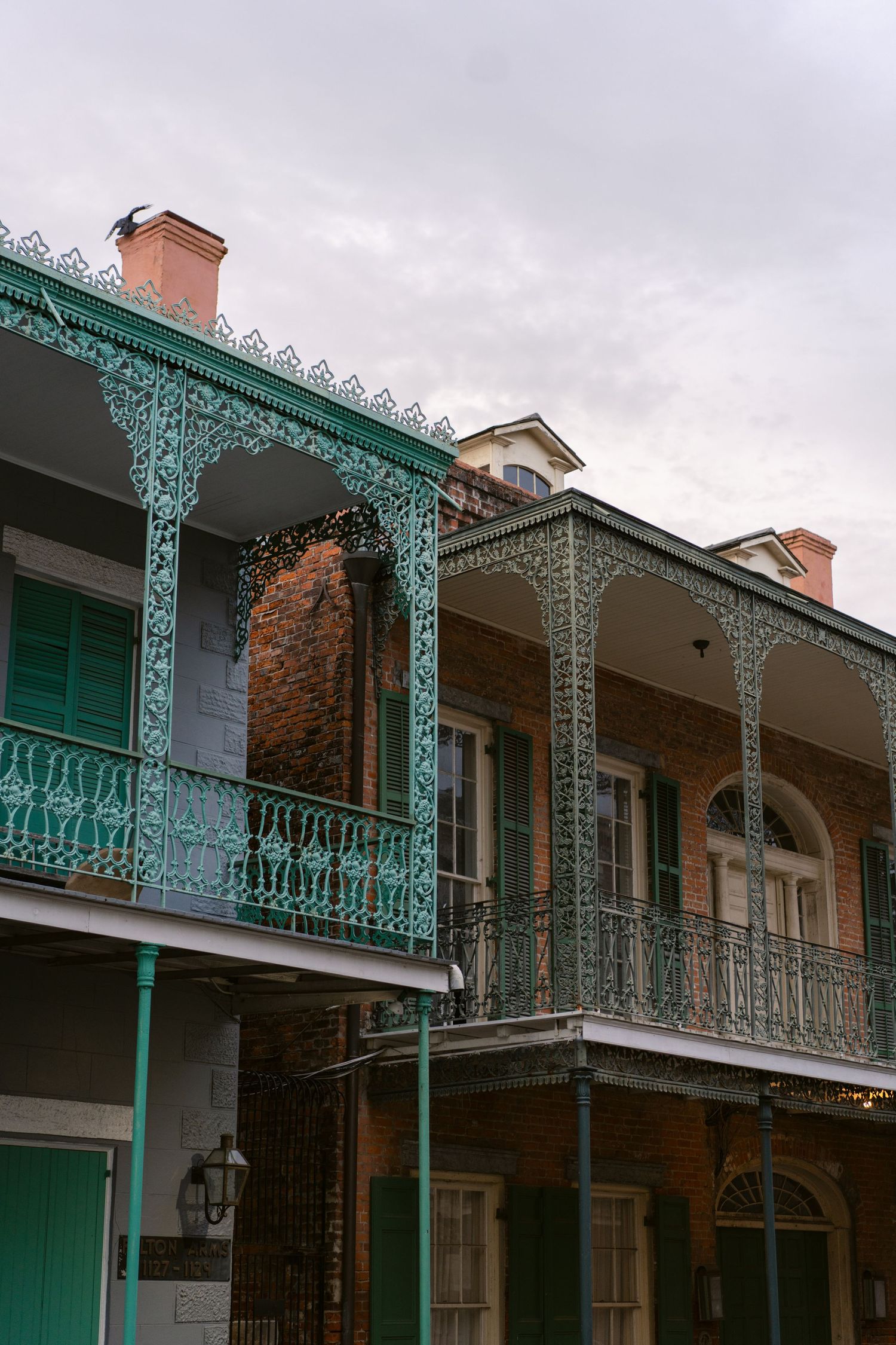 Historic New Orleans building with ornate turquoise ironwork balconies and columns.