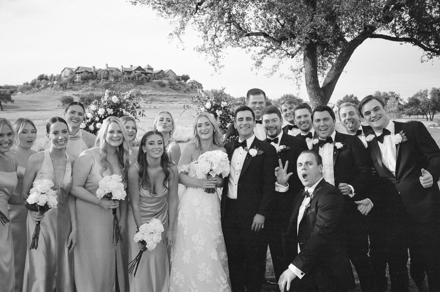 Wedding party in formal attire gathered outdoors for a group photo.