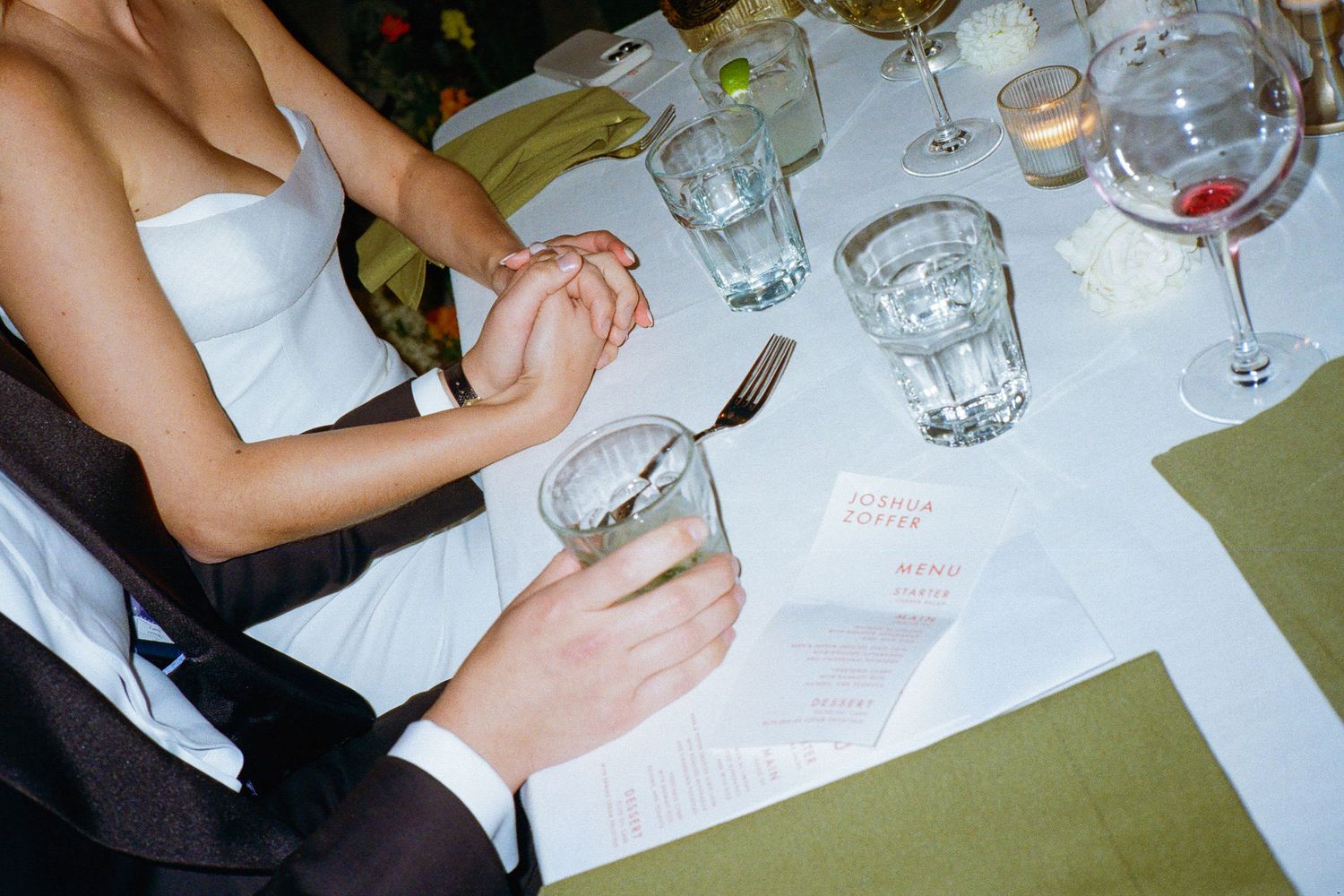 Overhead view of formal place settings with wine glasses and hands holding documents at a wedding reception.