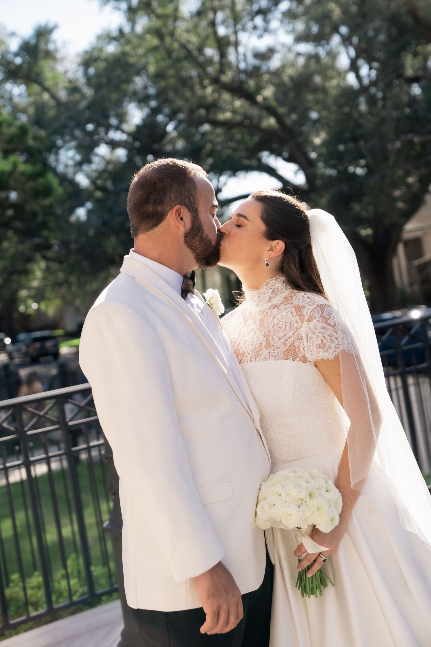 Newlyweds share an intimate moment outdoors with bride holding white bouquet.