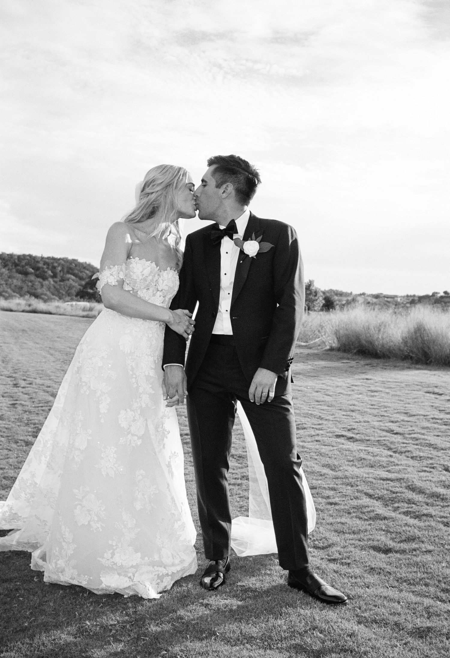 A romantic wedding couple poses together in black and white photos on a grassy outdoor field.