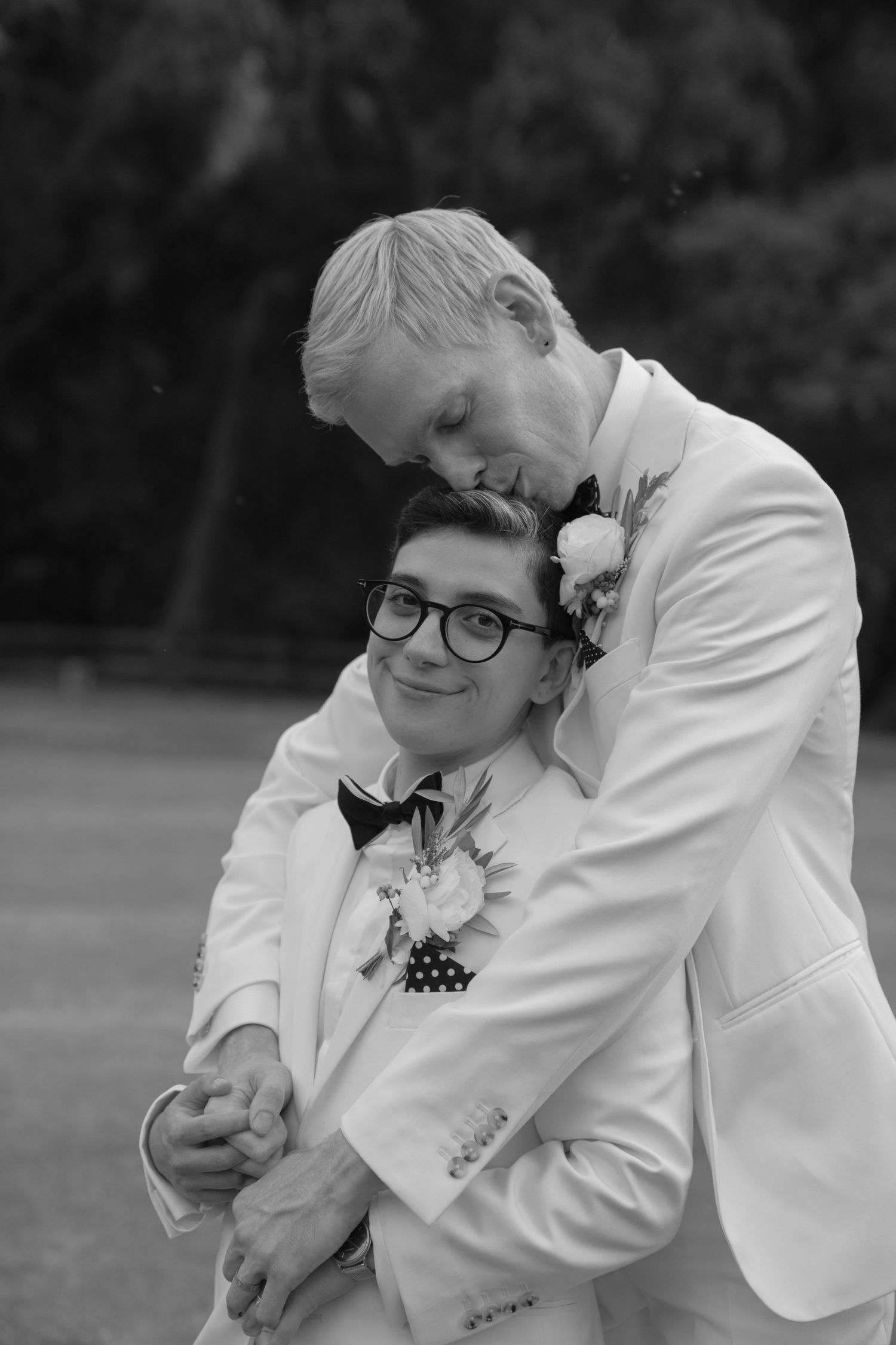 A tender black and white portrait of a couple in matching white tuxedos.