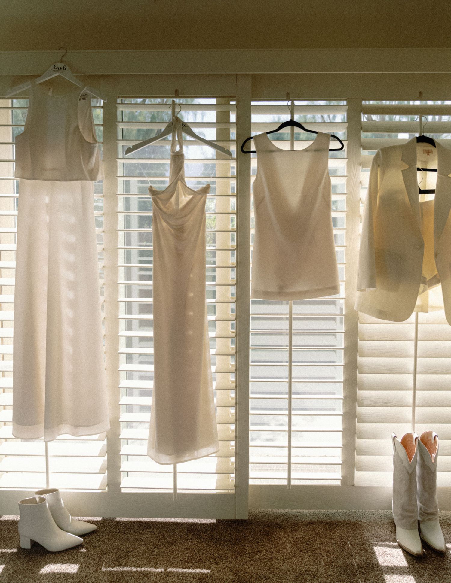 White clothing items hanging on hangers against a window with shutters.