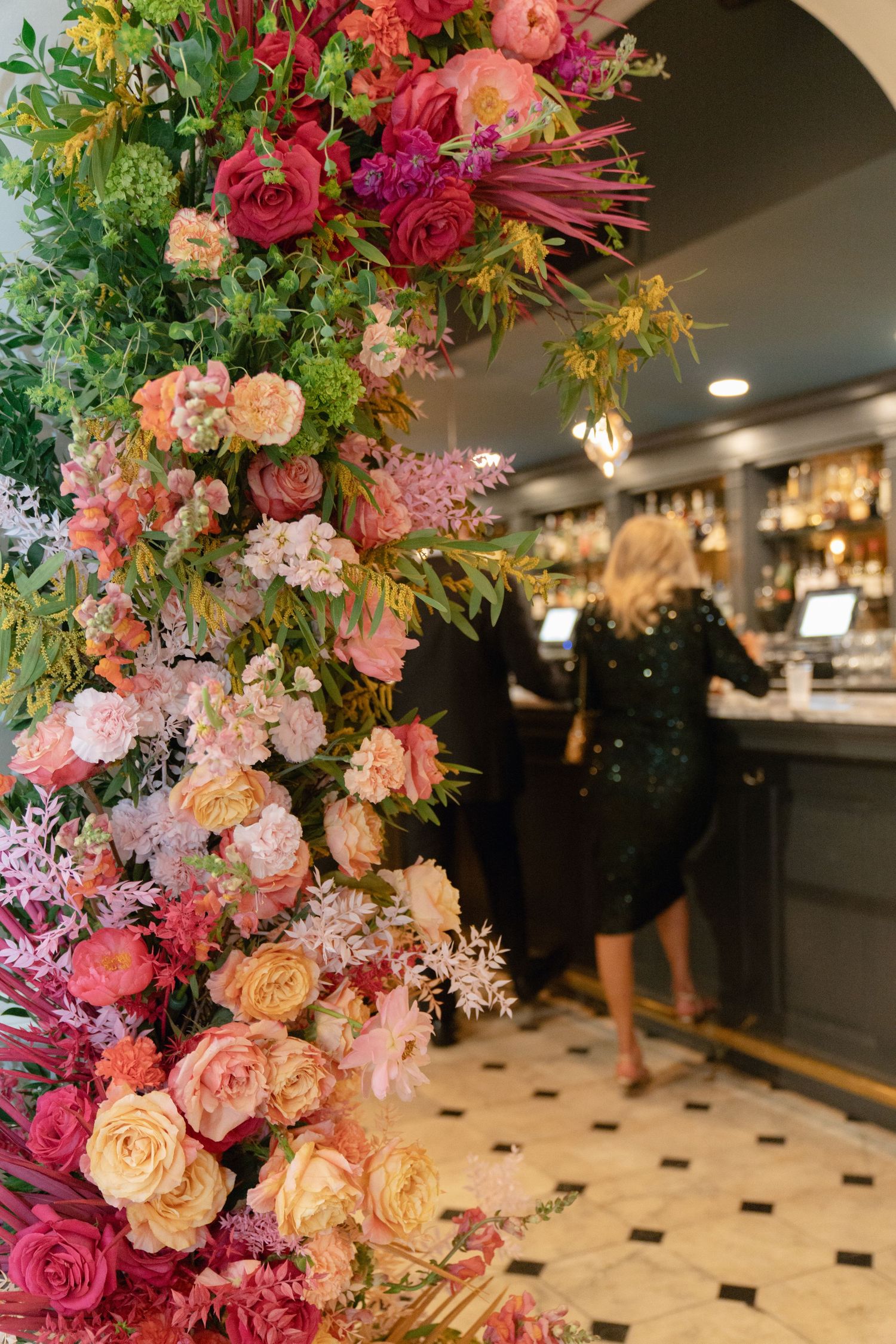 Luxurious floral arrangements featuring pink, coral and peach roses with greenery accent a reception space.