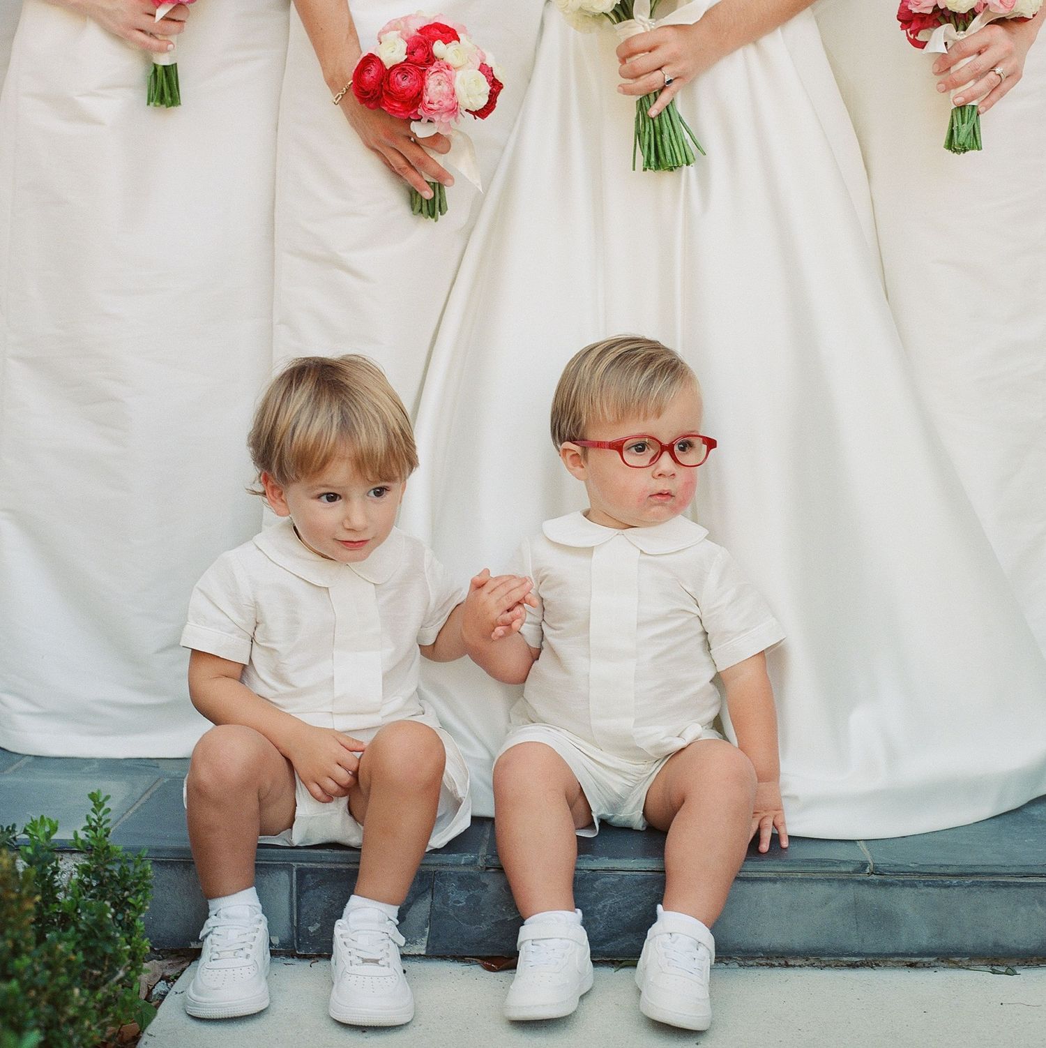 Children in white outfits sitting together on a bench holding red and white flowers.