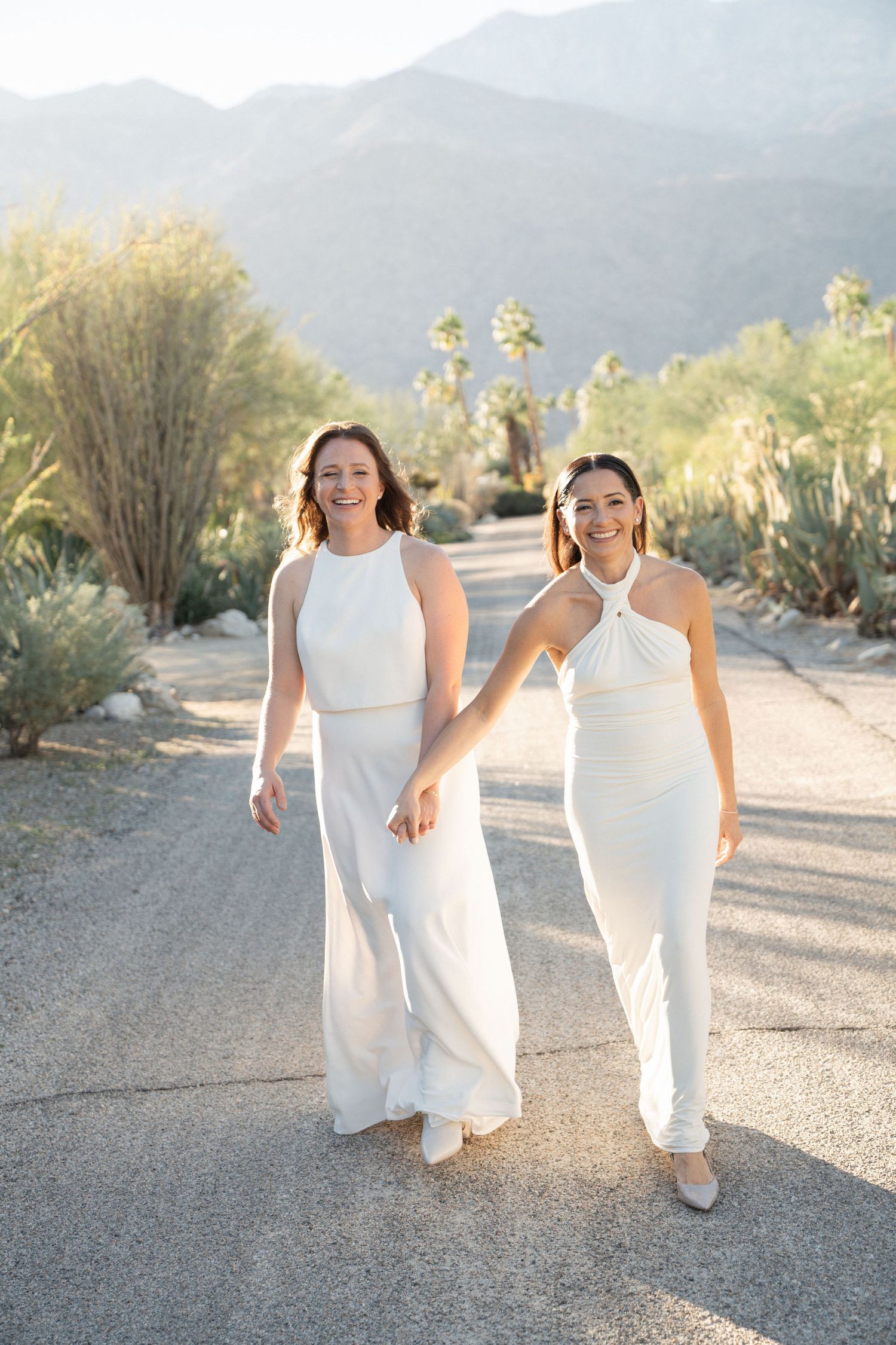 Two people in white outfits walking together on a desert path during golden hour.