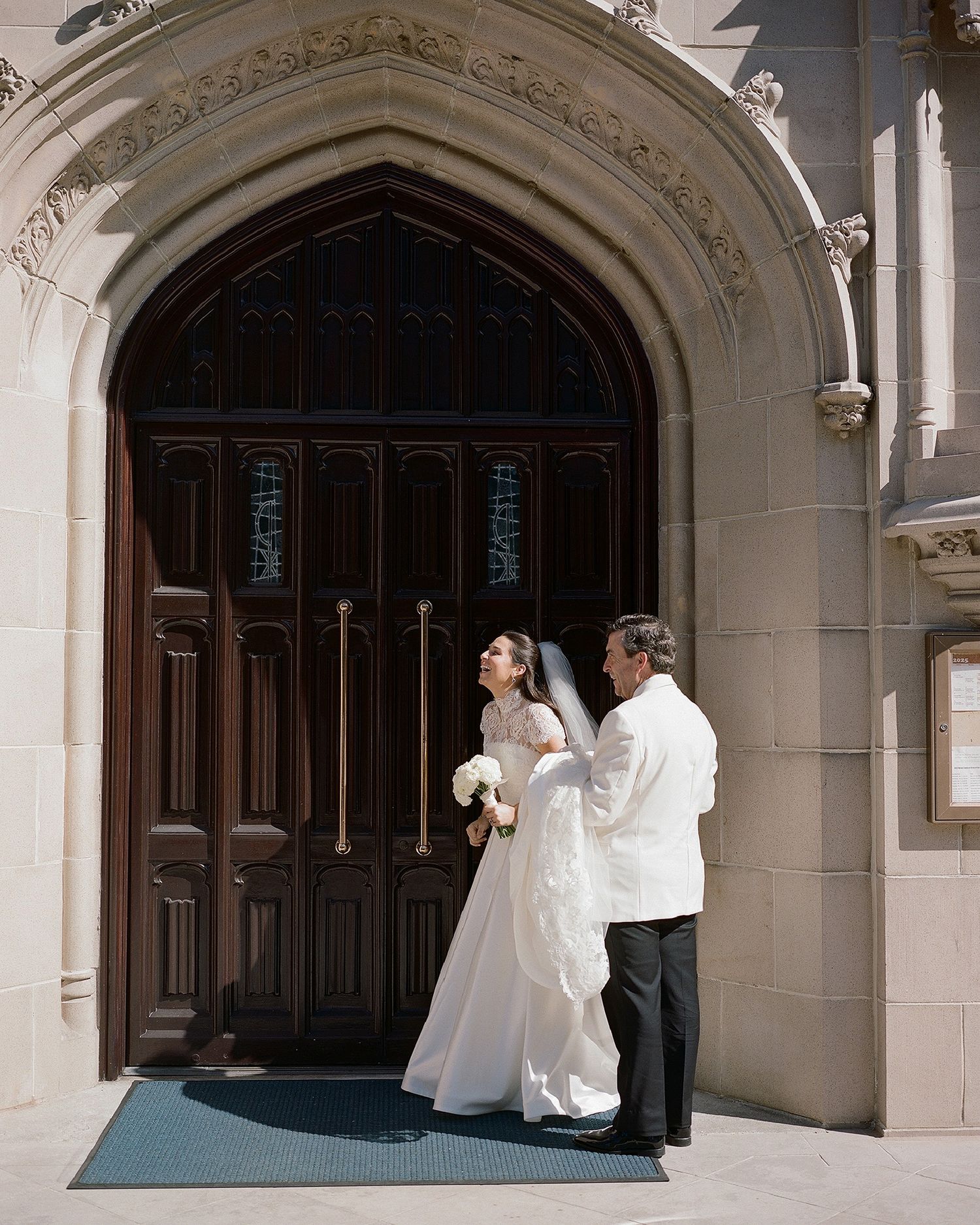 A wedding couple stands beneath an ornate gothic archway entrance.