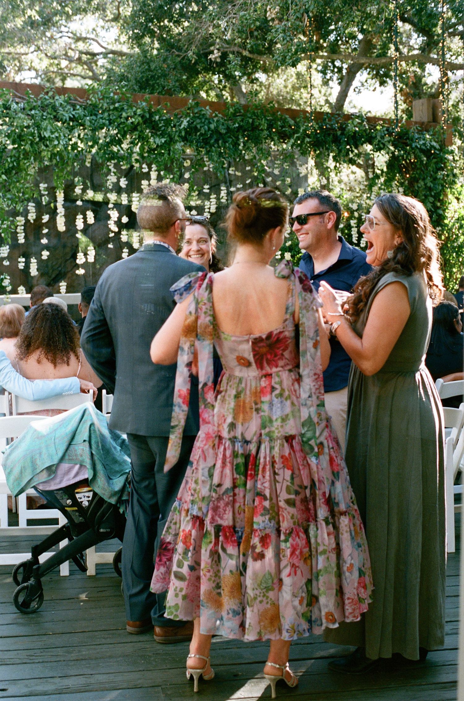 Wedding guests in floral dresses mingling at an outdoor reception.