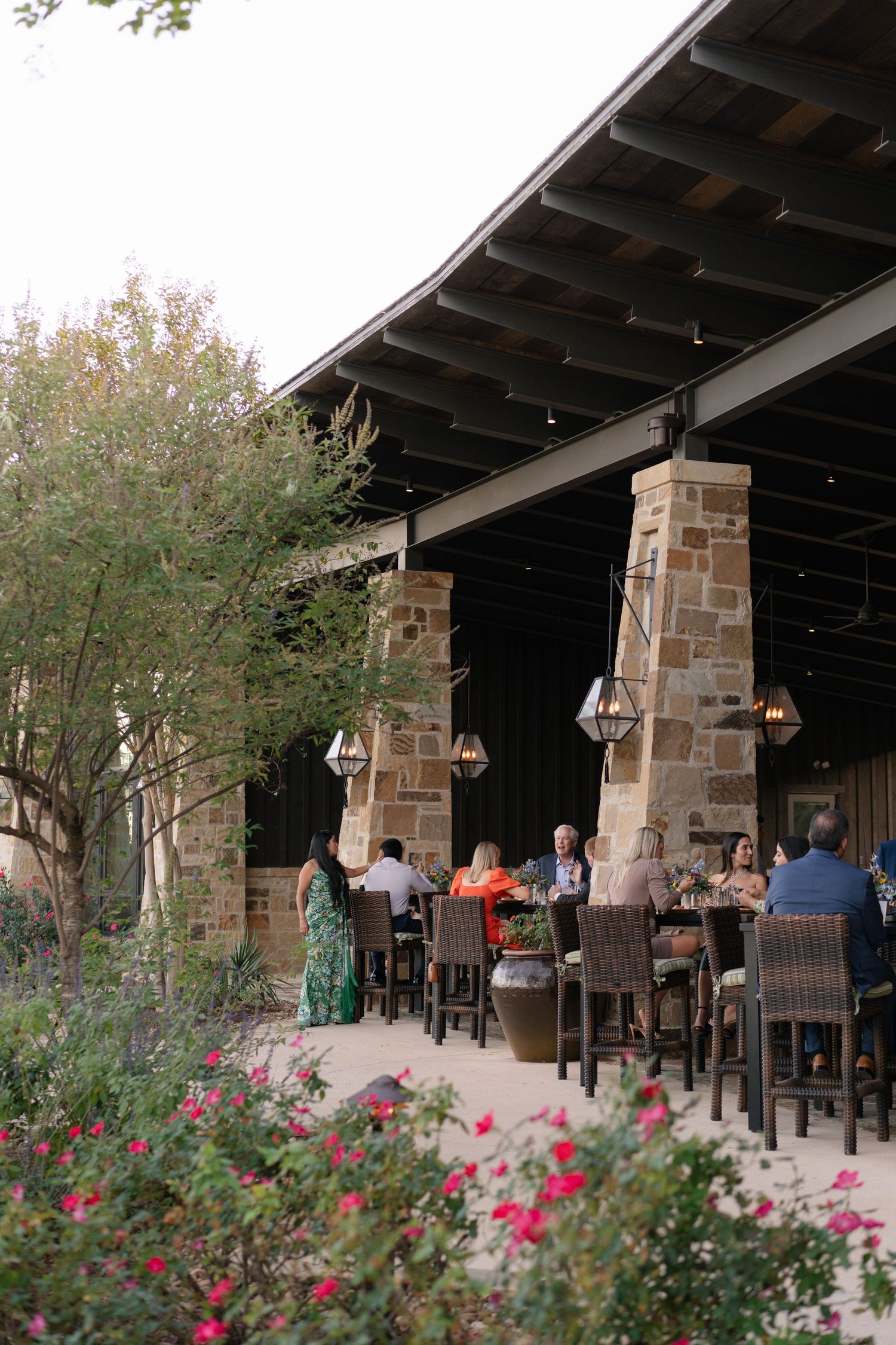 Outdoor patio dining area with stone columns and pink flowers blooming in the garden.