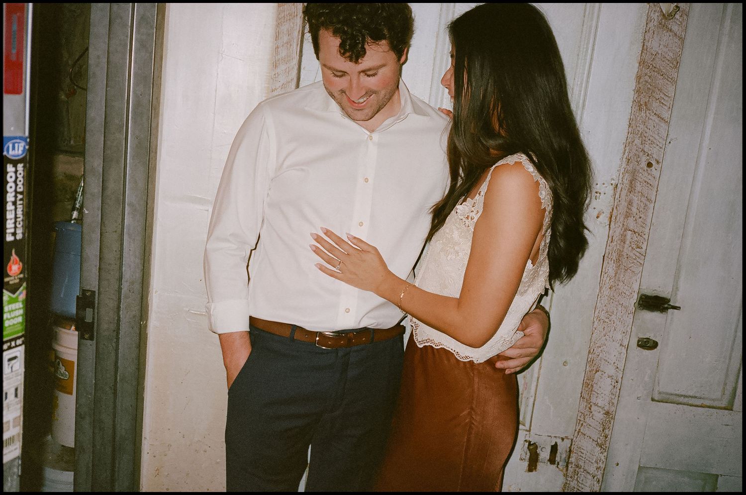 A couple shares an intimate moment, the man in a white shirt and the woman in a lace top and brown skirt.