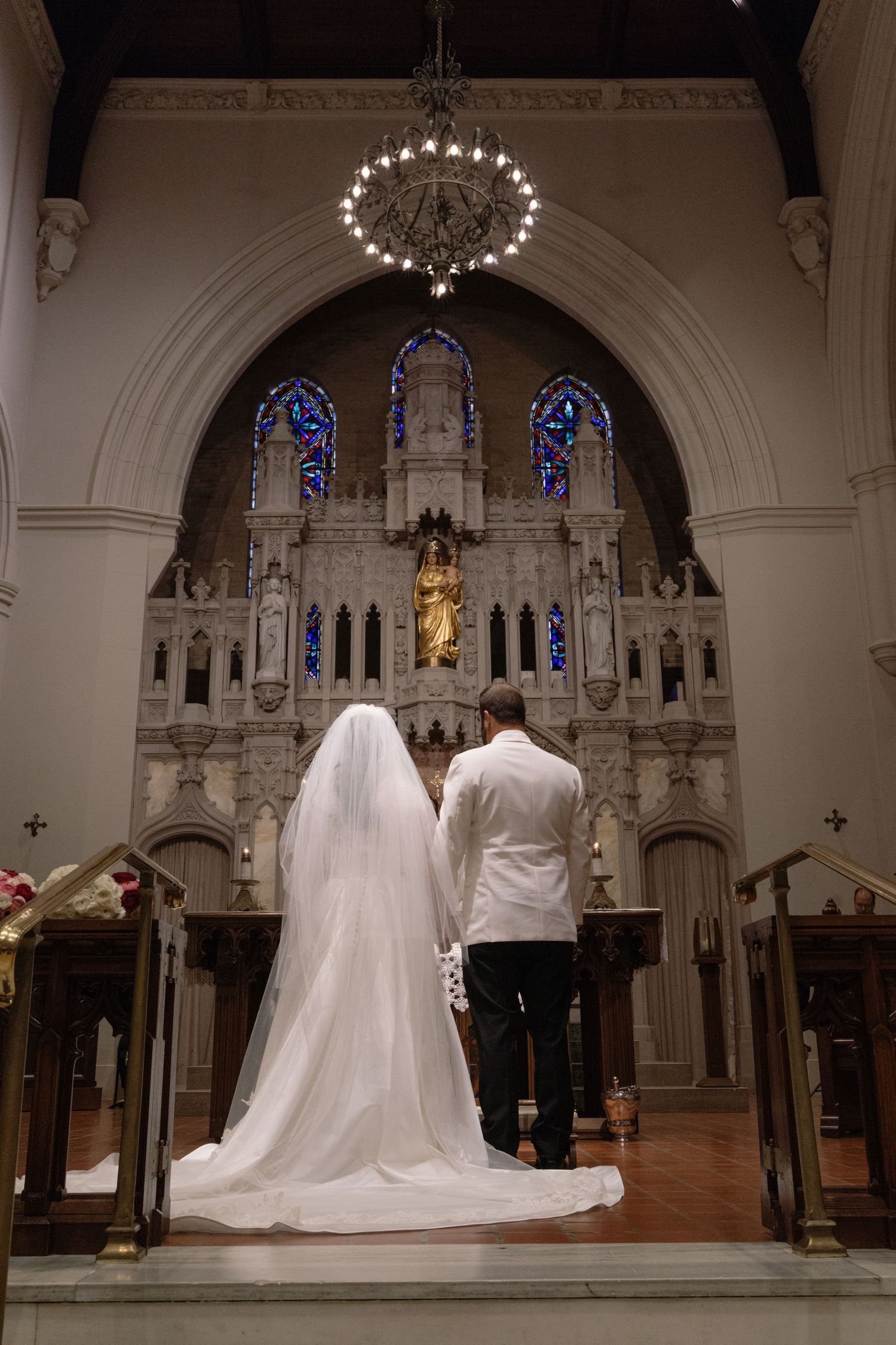 A couple stands at the altar of an ornate church with stained glass windows and gothic architecture.
