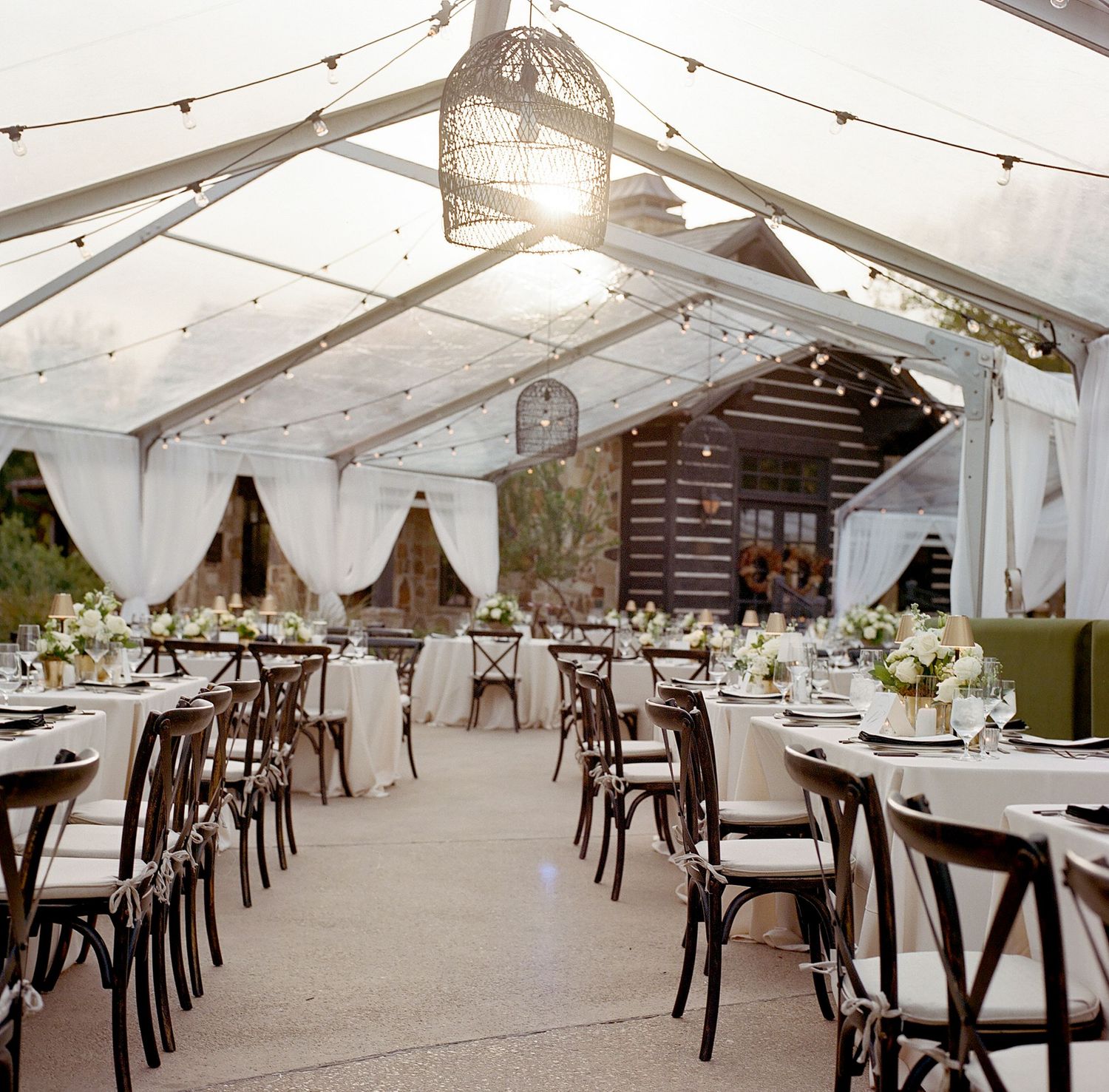 Elegant tented wedding reception with string lights, chandeliers and cross-back chairs.