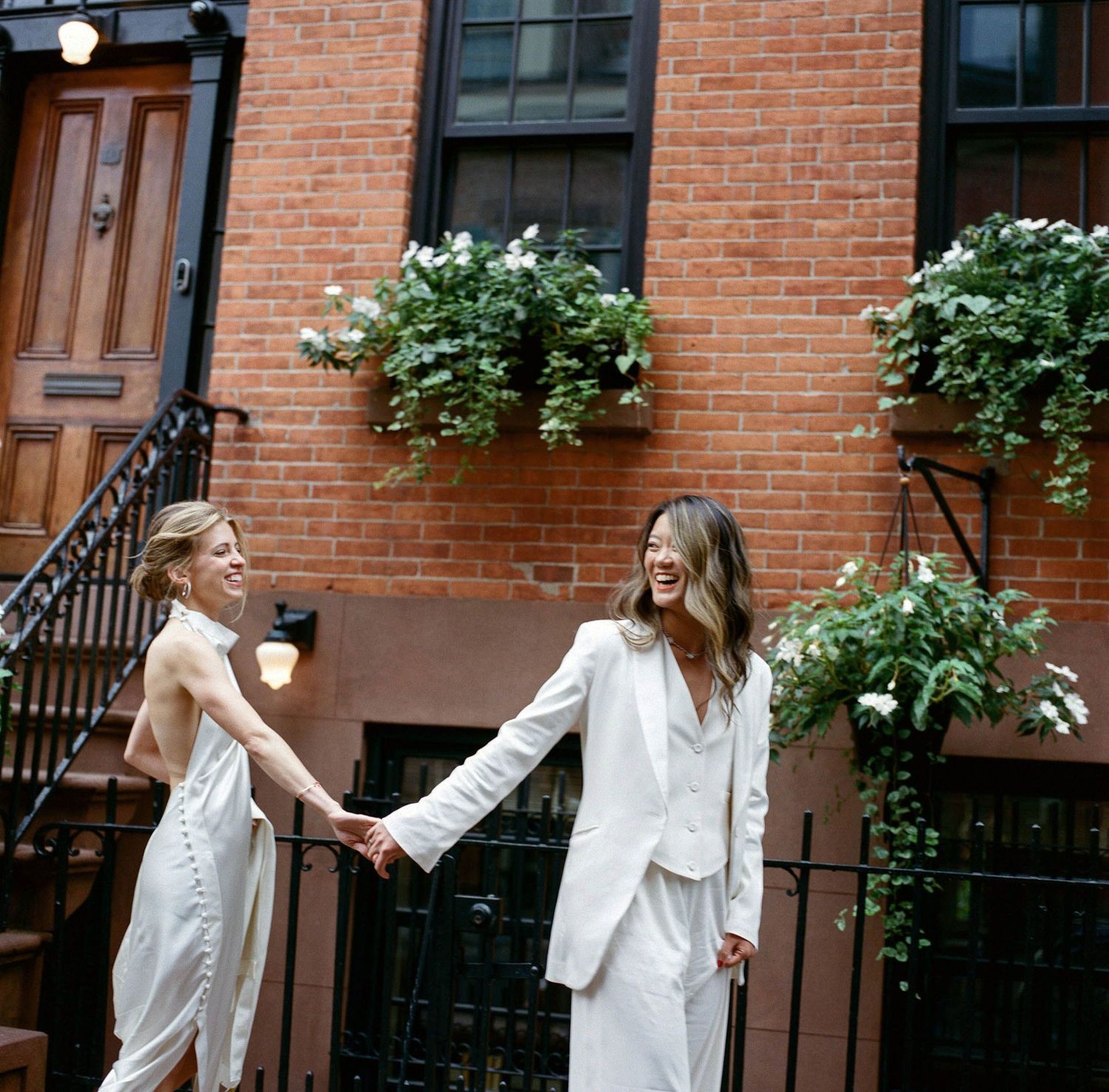 Two people in white outfits dance playfully on a brownstone-lined street.