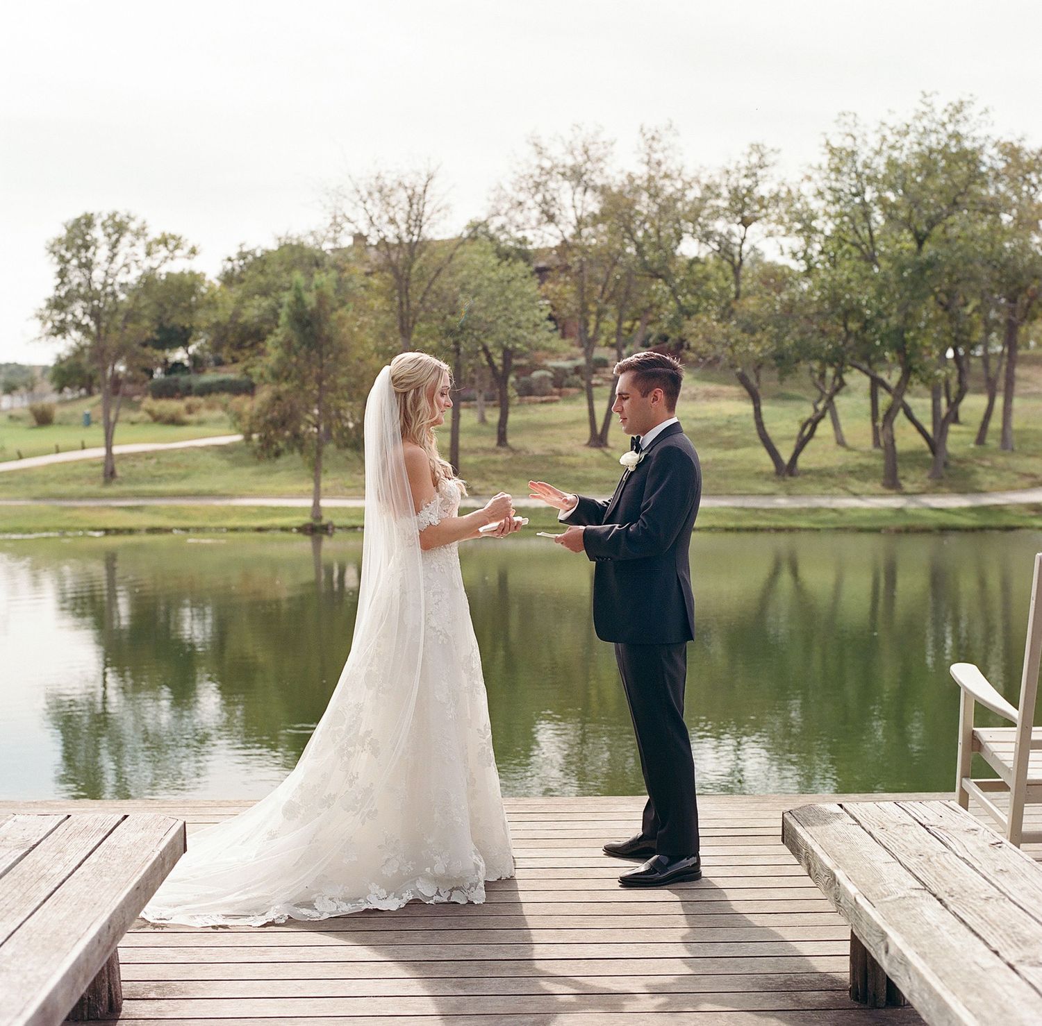 Wedding couple standing on a wooden dock overlooking a serene lake.