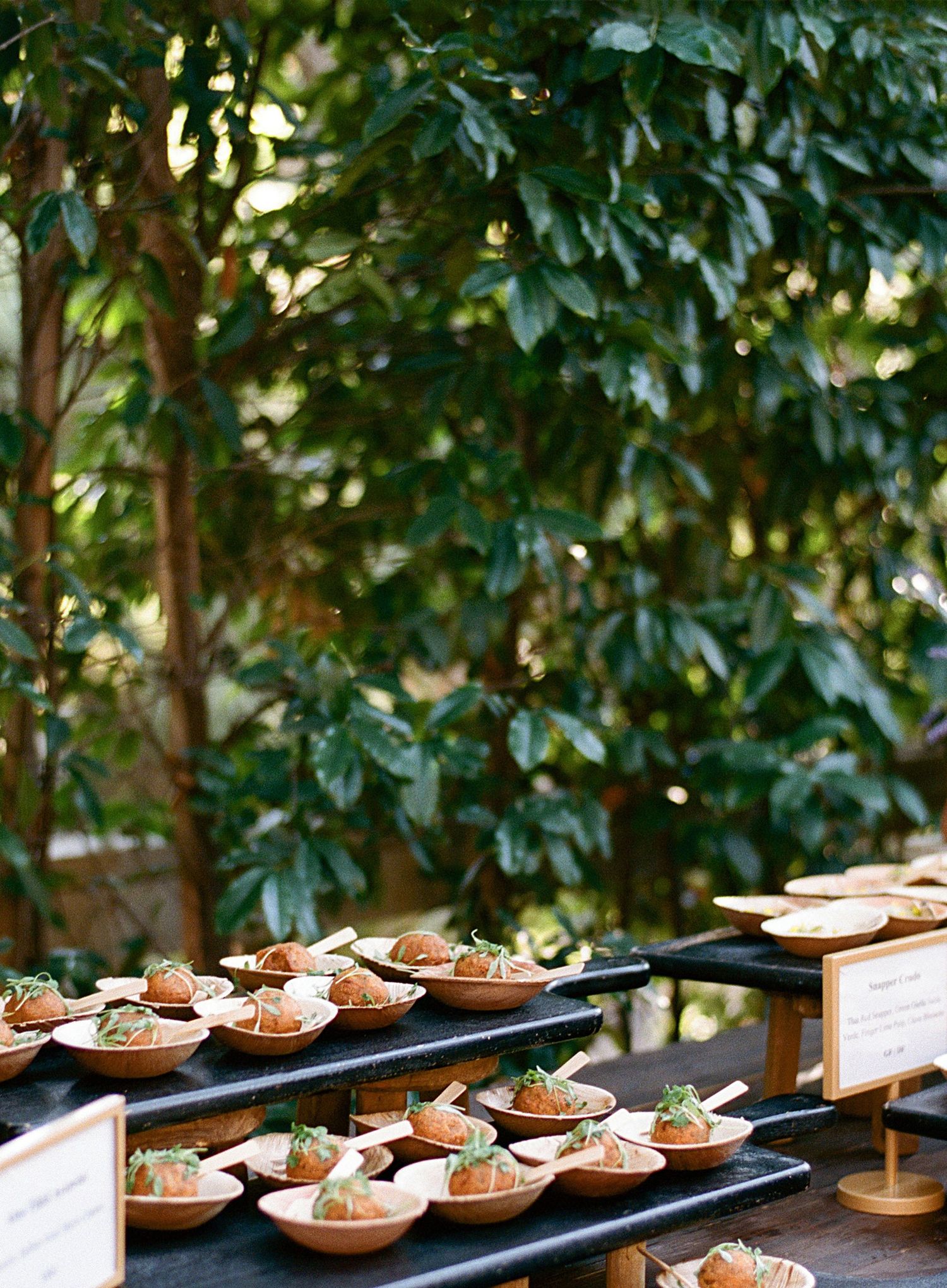 Rows of elegant appetizers displayed on wooden serving platters at an outdoor event.