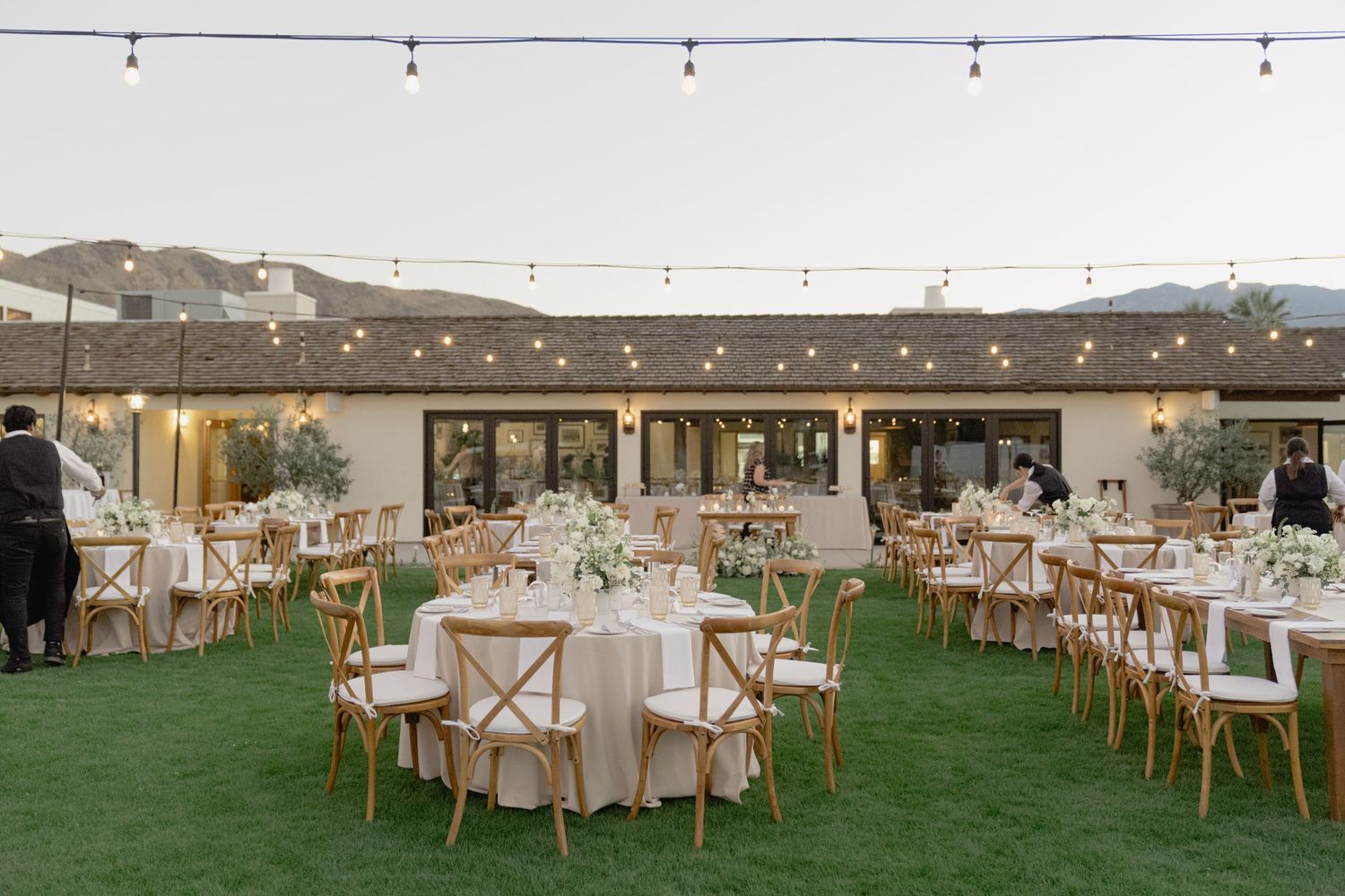 Outdoor wedding reception setup with round tables and string lights creating an elegant atmosphere.