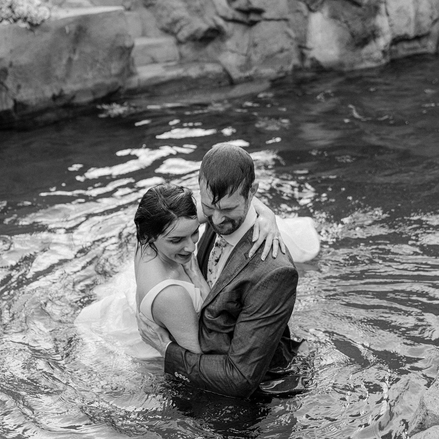 A couple shares an intimate moment while swimming in formal attire.