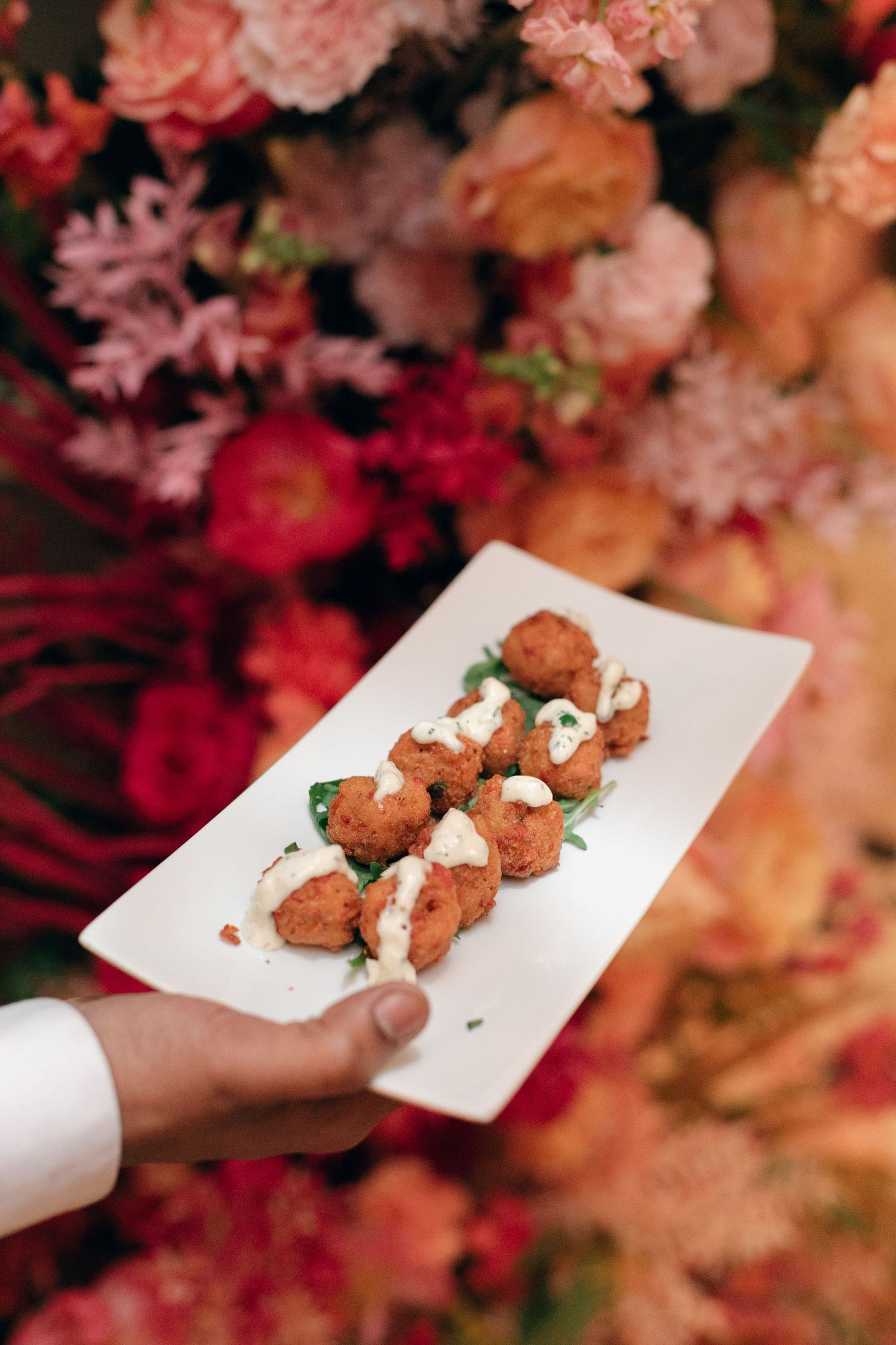 Small appetizers being served on white plates against a backdrop of pink and coral floral arrangements.