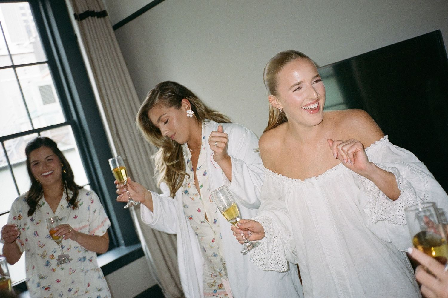 Joyful pre-wedding celebration with women in white robes holding champagne glasses.
