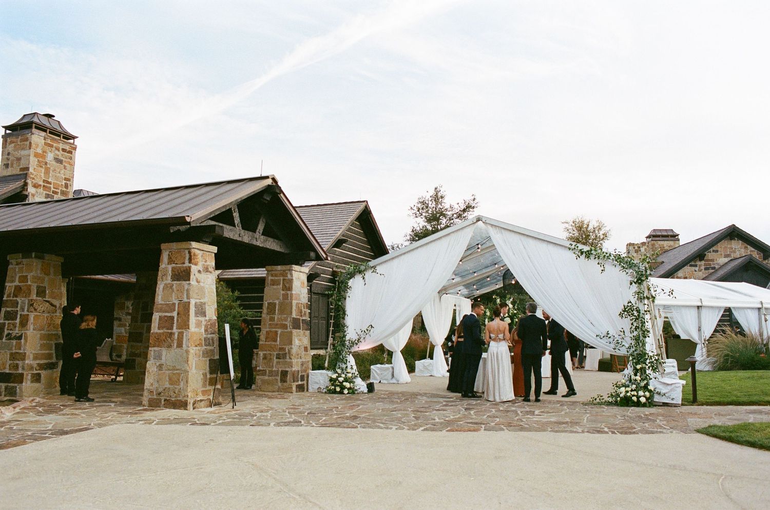 Outdoor wedding venue with stone buildings and white tent setup visible in panoramic view.