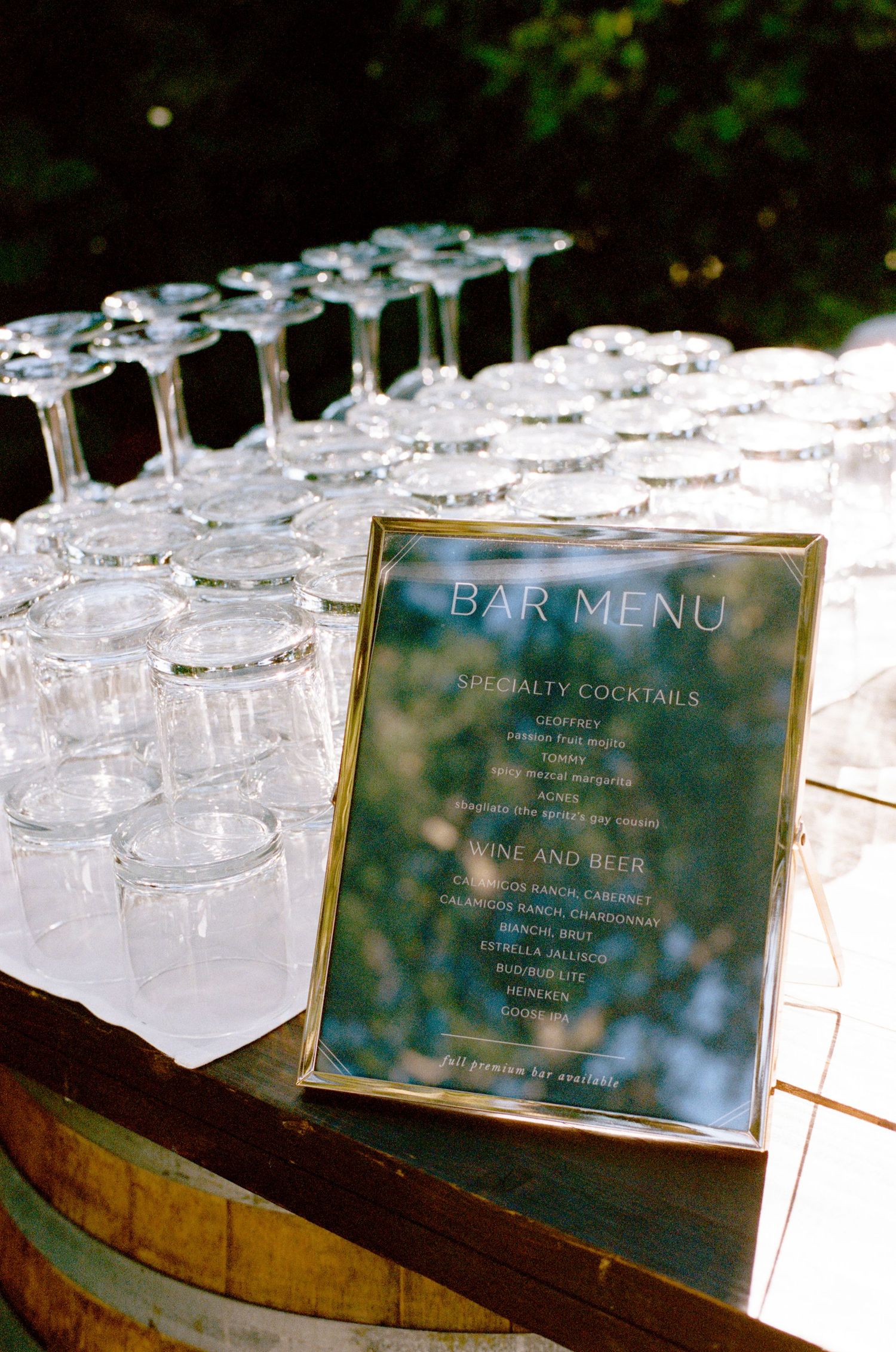 Empty cocktail glasses lined up on a wooden bar with framed drink menus.