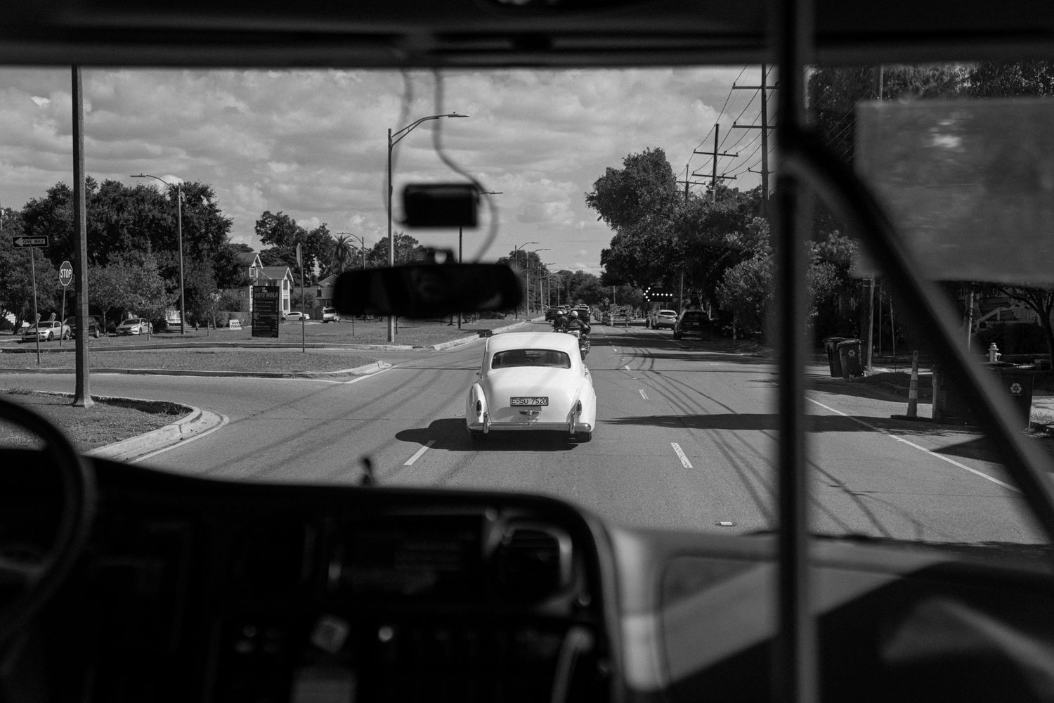 Black and white vintage-style photo of a car on a street viewed through a windshield.