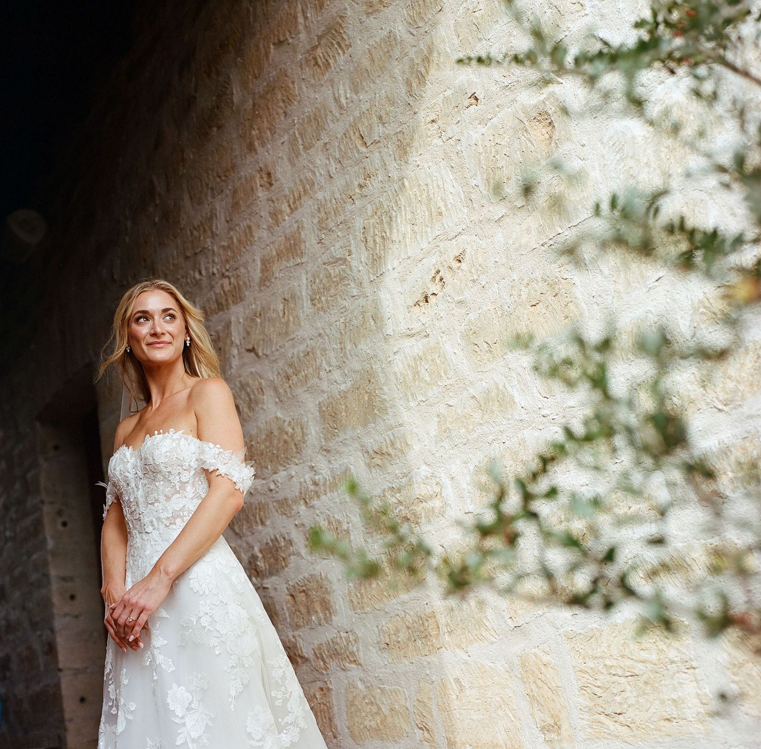 Wedding dress with delicate lace details photographed against a stone wall.
