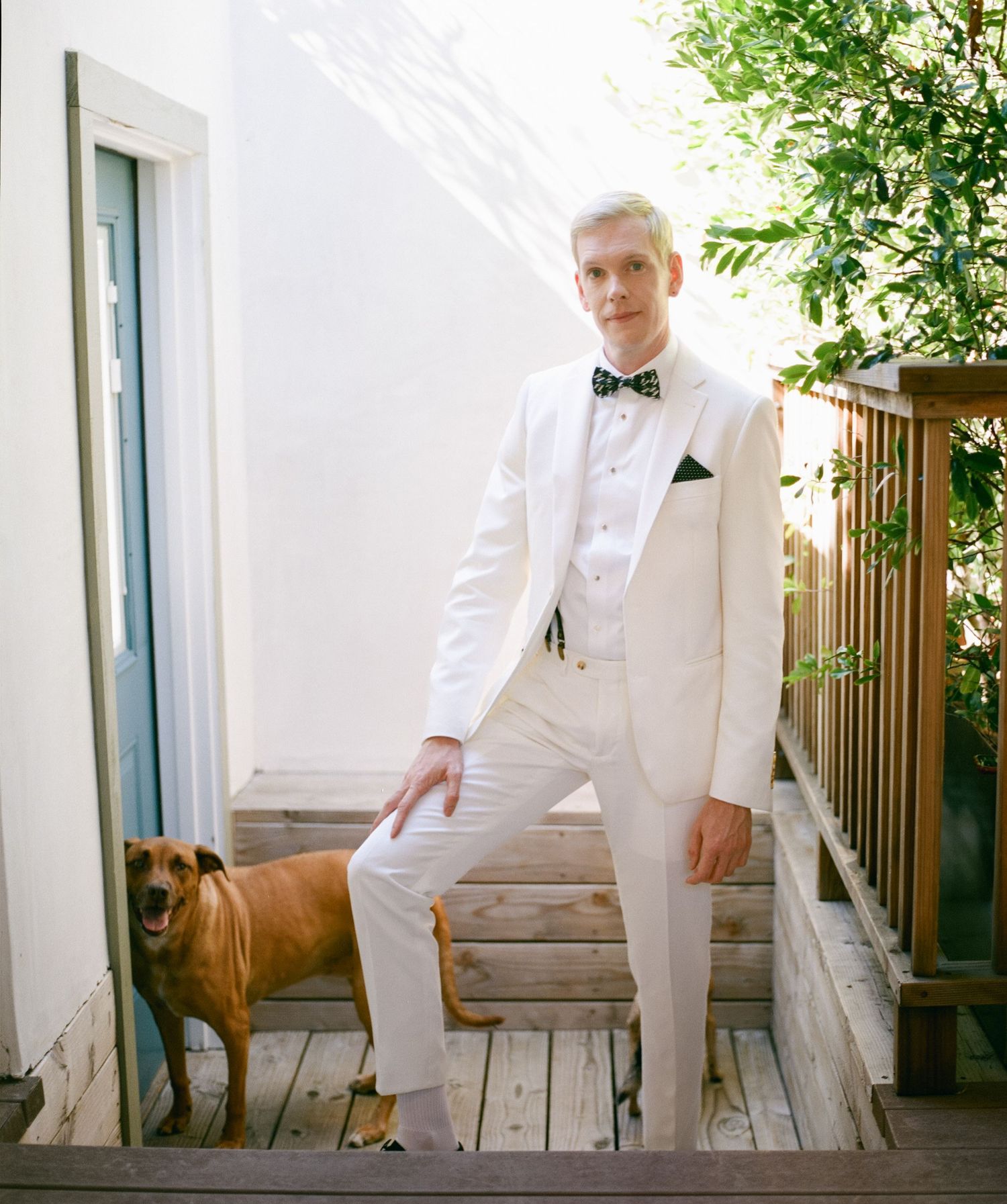 Person in white formal attire poses on wooden deck outdoors.
