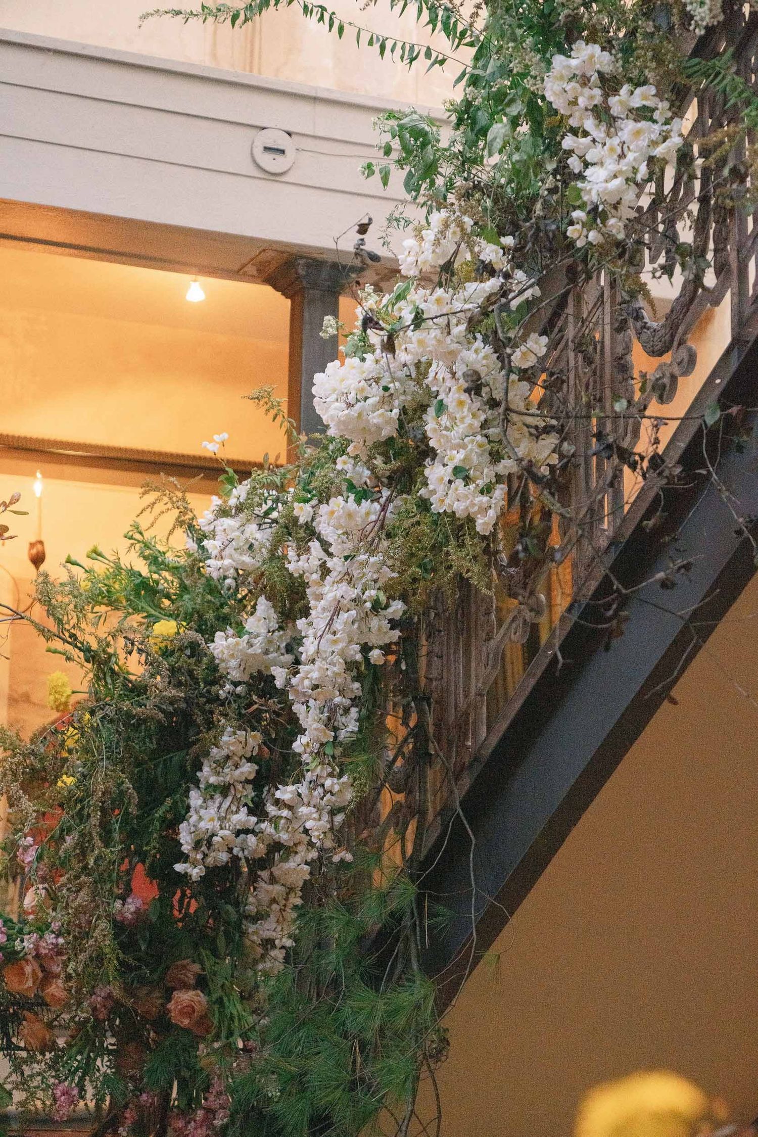 White floral arrangements cascade down a modern staircase railing in an indoor space.