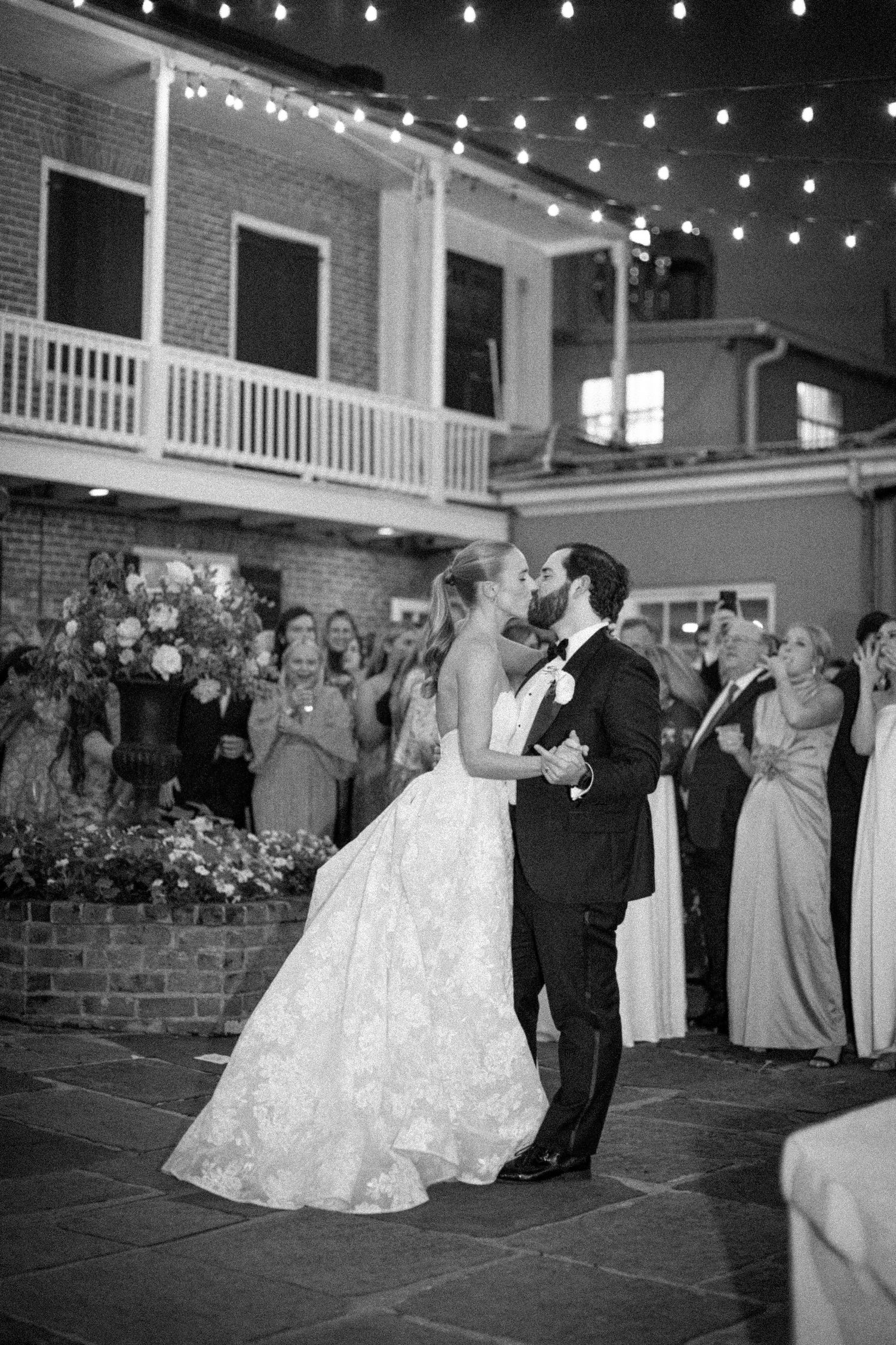 Couples dancing at an evening wedding reception under string lights in a historic brick venue.