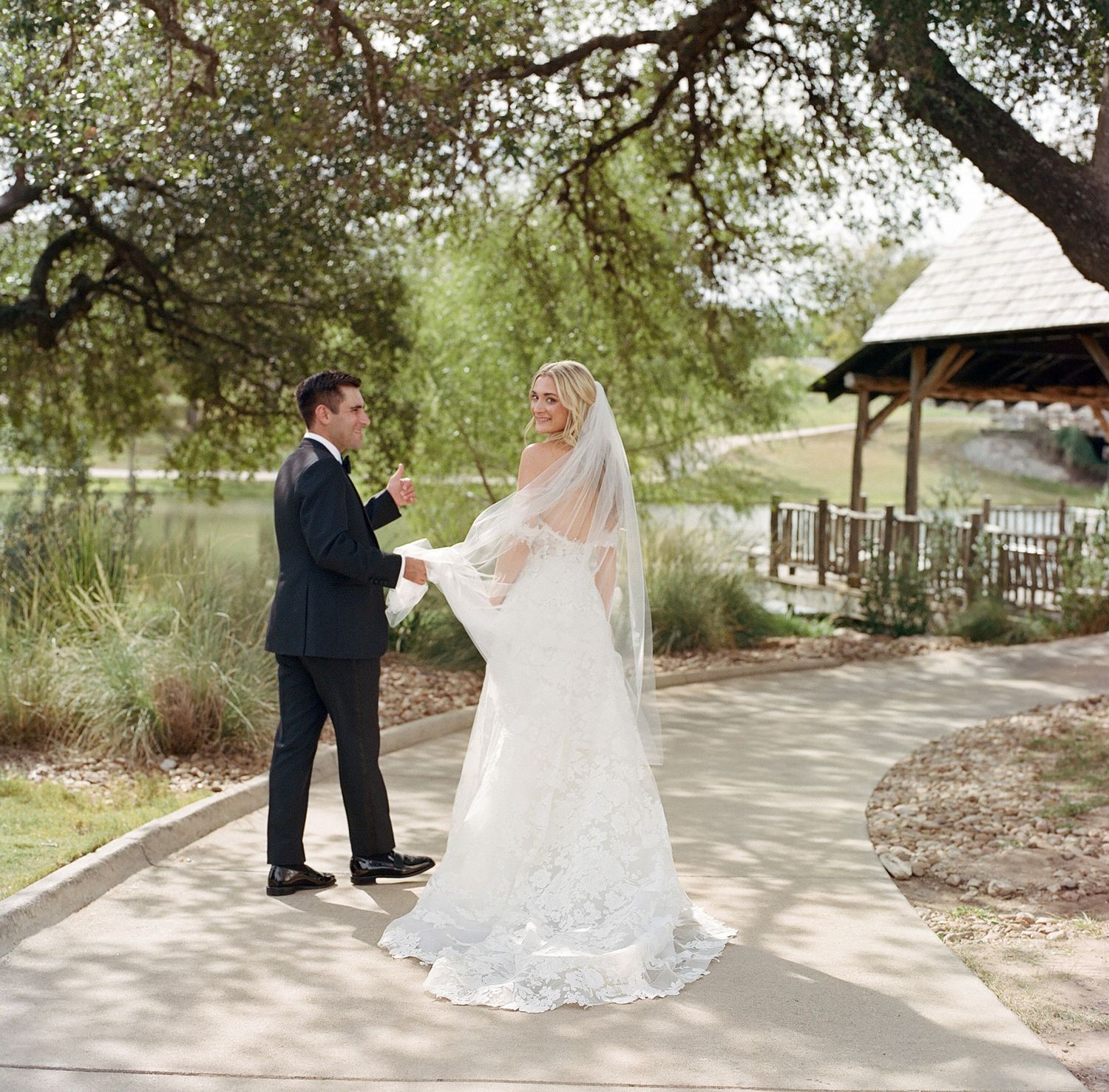 Wedding couple walking along a tree-lined pathway during an outdoor ceremony.