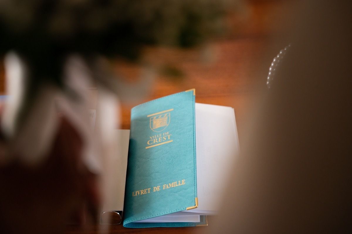 A light blue passport or travel document stands upright against a blurred warm-toned background.