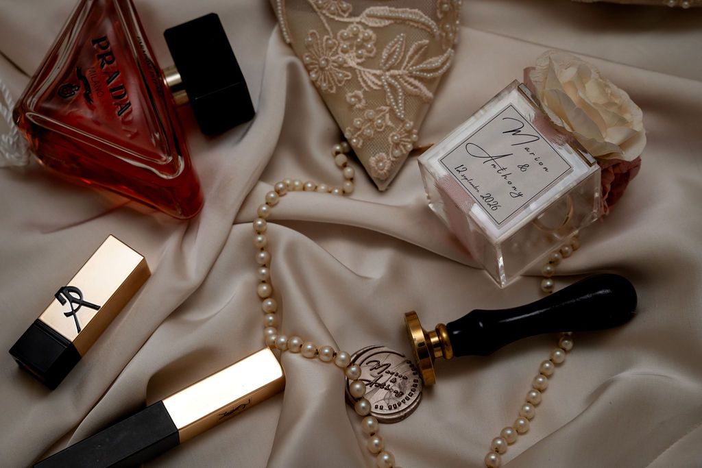Luxury beauty flatlay with YSL lipstick, red perfume bottle, pearl necklace, and fragrance on silk fabric.