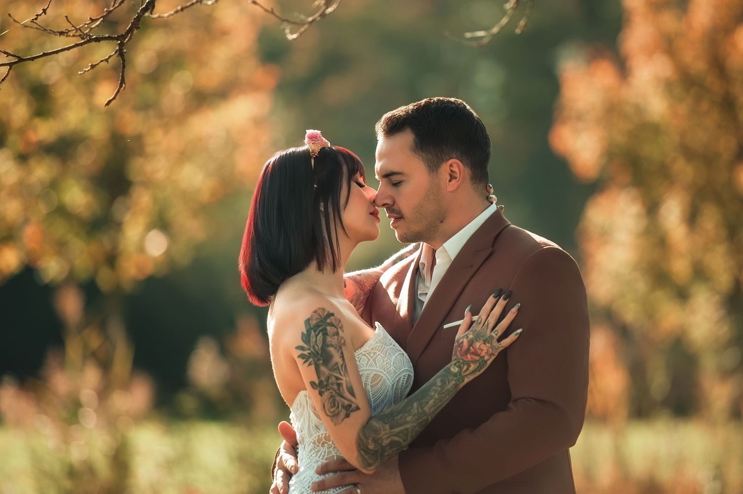 A romantic couple embraces outdoors during golden hour with autumn foliage in the background.