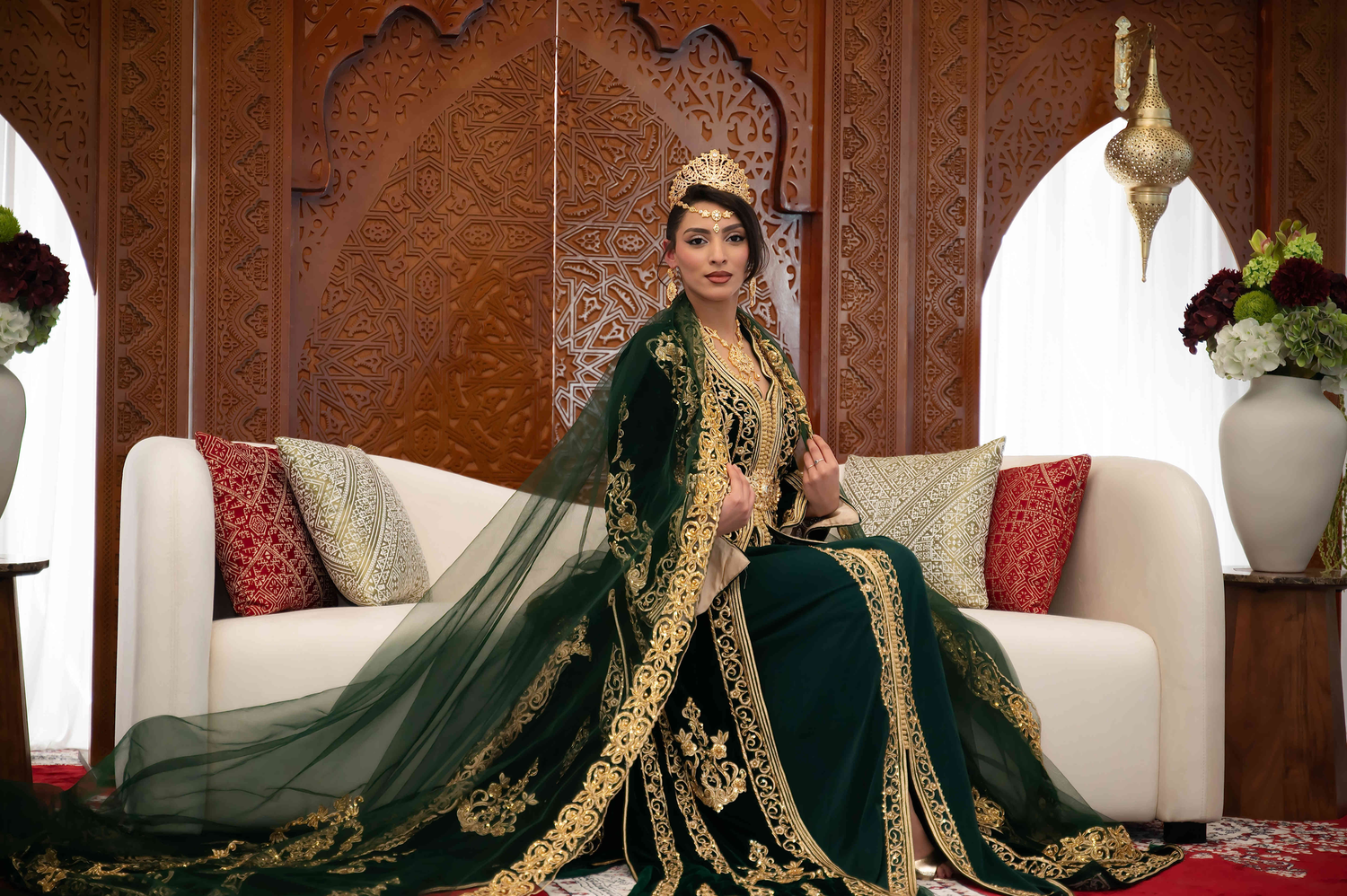 Elegant emerald green and gold traditional Moroccan dress with intricate embroidery displayed in a luxurious interior setting.
