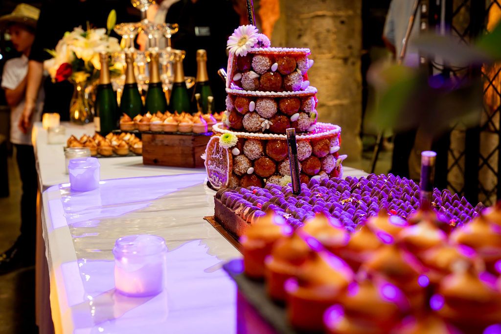 Elegant wedding dessert table with tiered floral cake, purple candles, and assorted pastries at a festive reception.