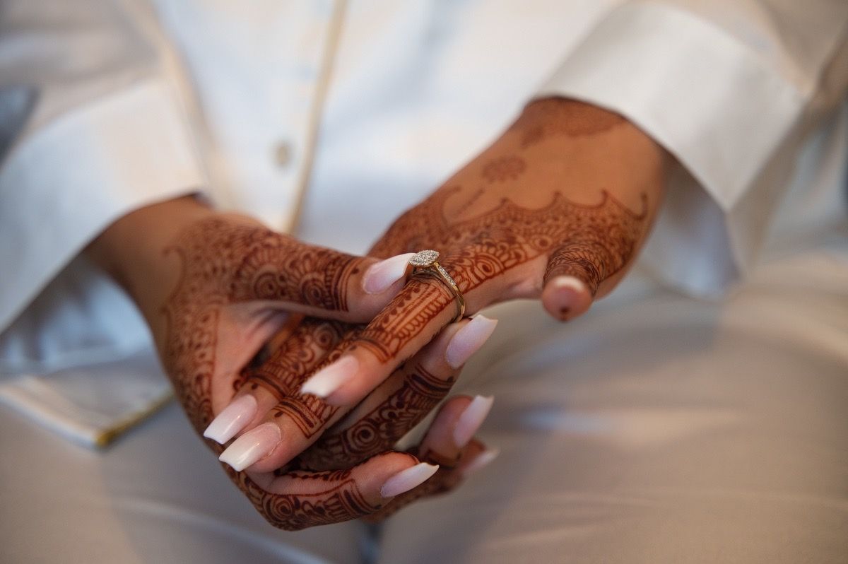 Close-up of intricate henna designs on hands with white fabric in background.