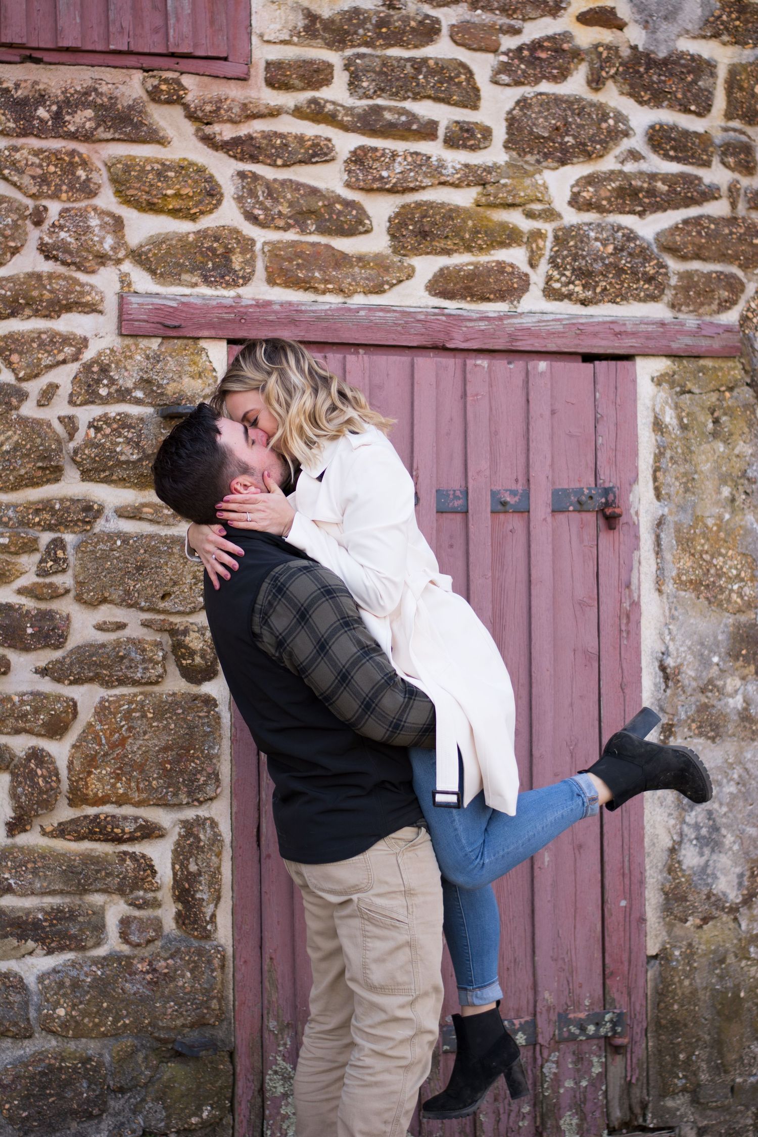 Couple sharing a romantic kiss outside a rustic stone building with a weathered red door.