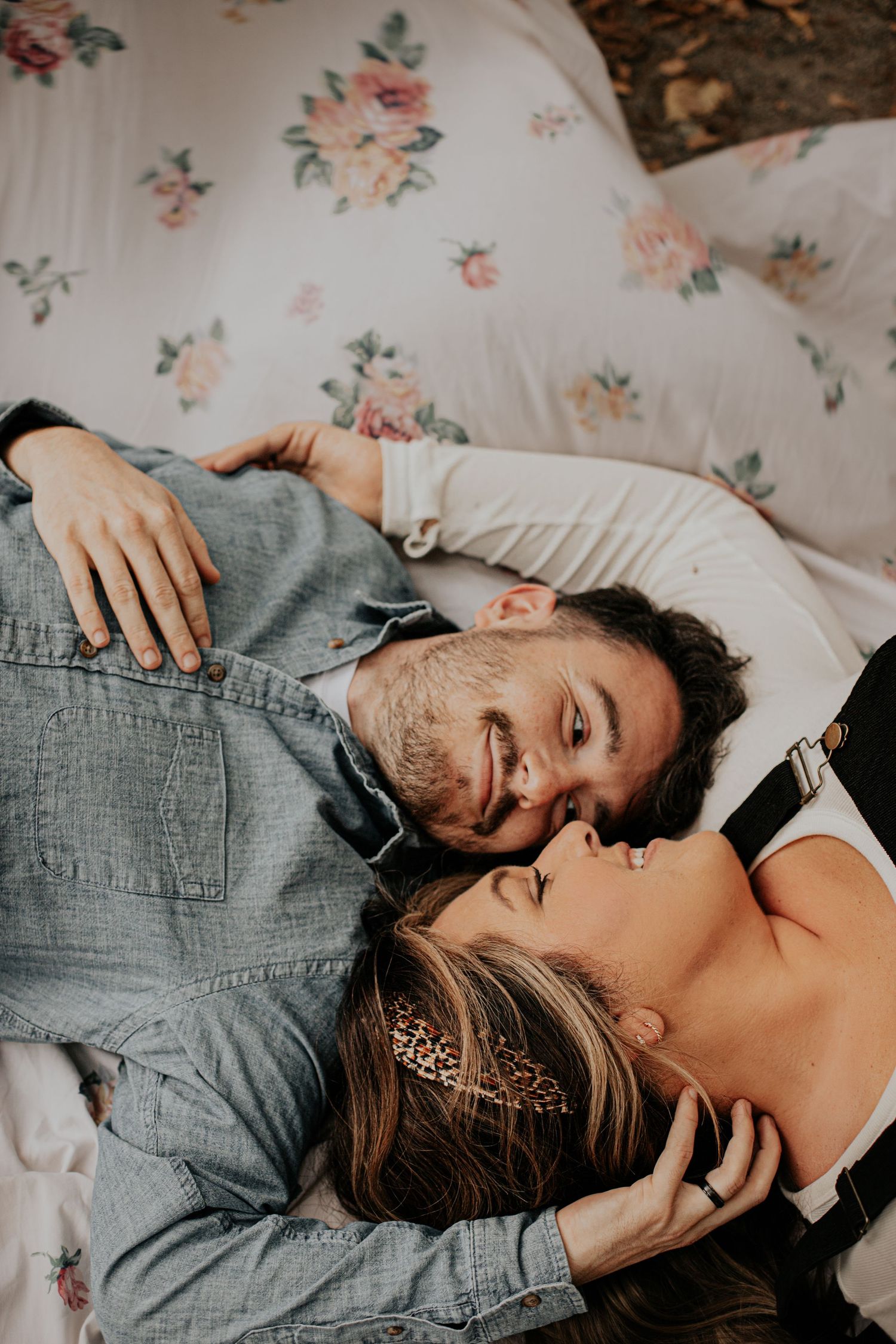 A couple lying on a floral blanket, sharing a tender moment as the man gazes lovingly at the smiling woman.